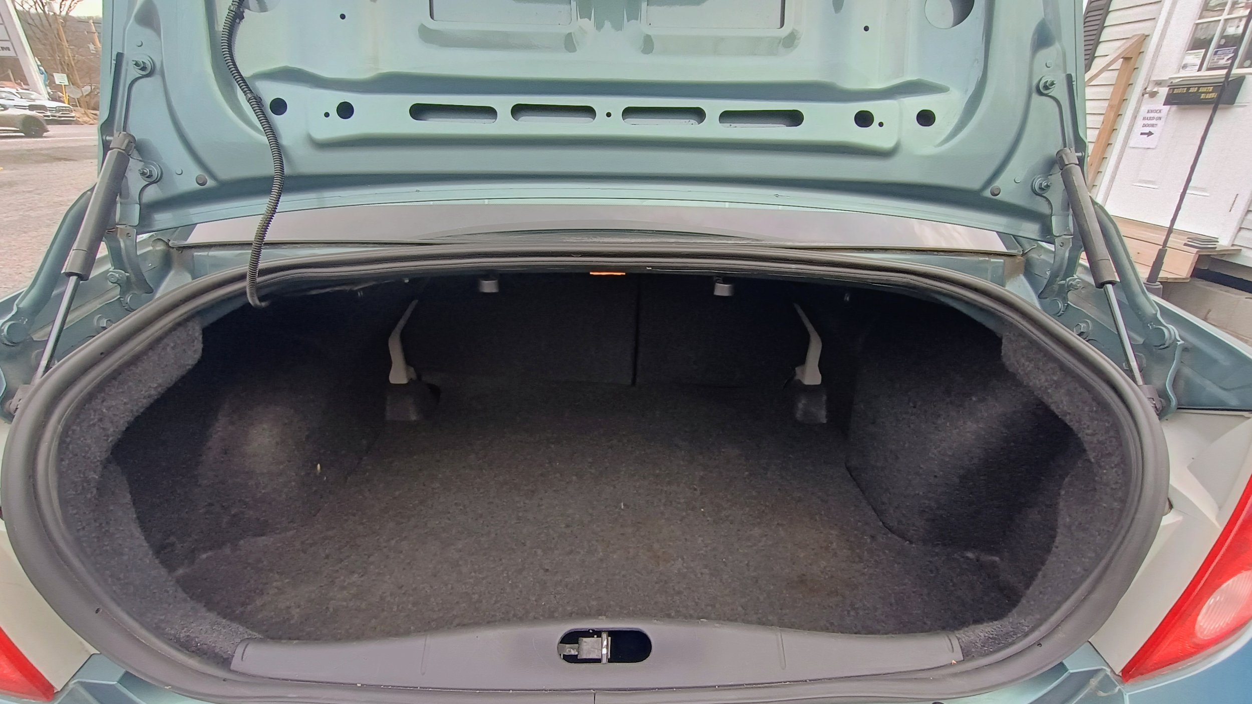Open car trunk showing the interior lined with dark fabric, with the back seats visible inside.
