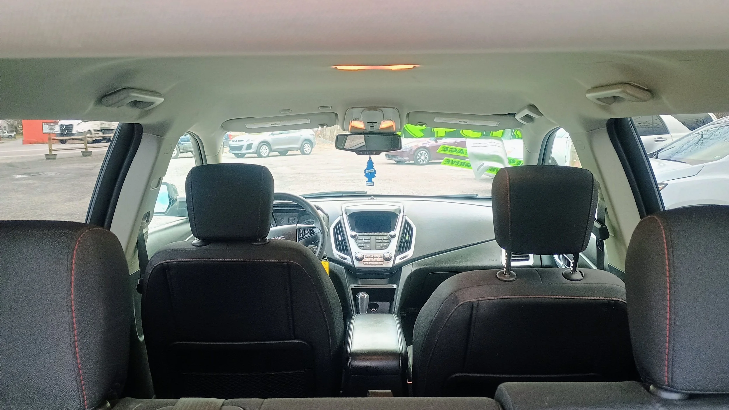 View of the interior of a vehicle from the back seat, showing the front seats, dashboard, steering wheel, and rearview mirror, with a parking lot outside.