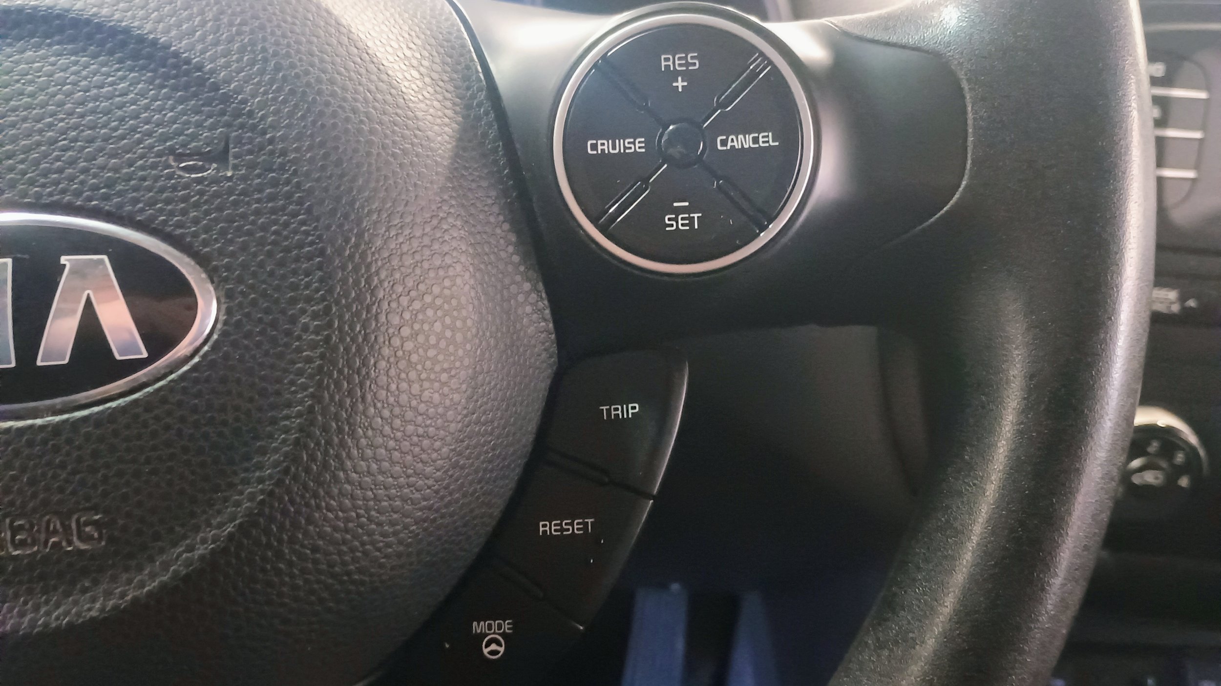 Close-up of a Kia car steering wheel with cruise control buttons and a trip control button.