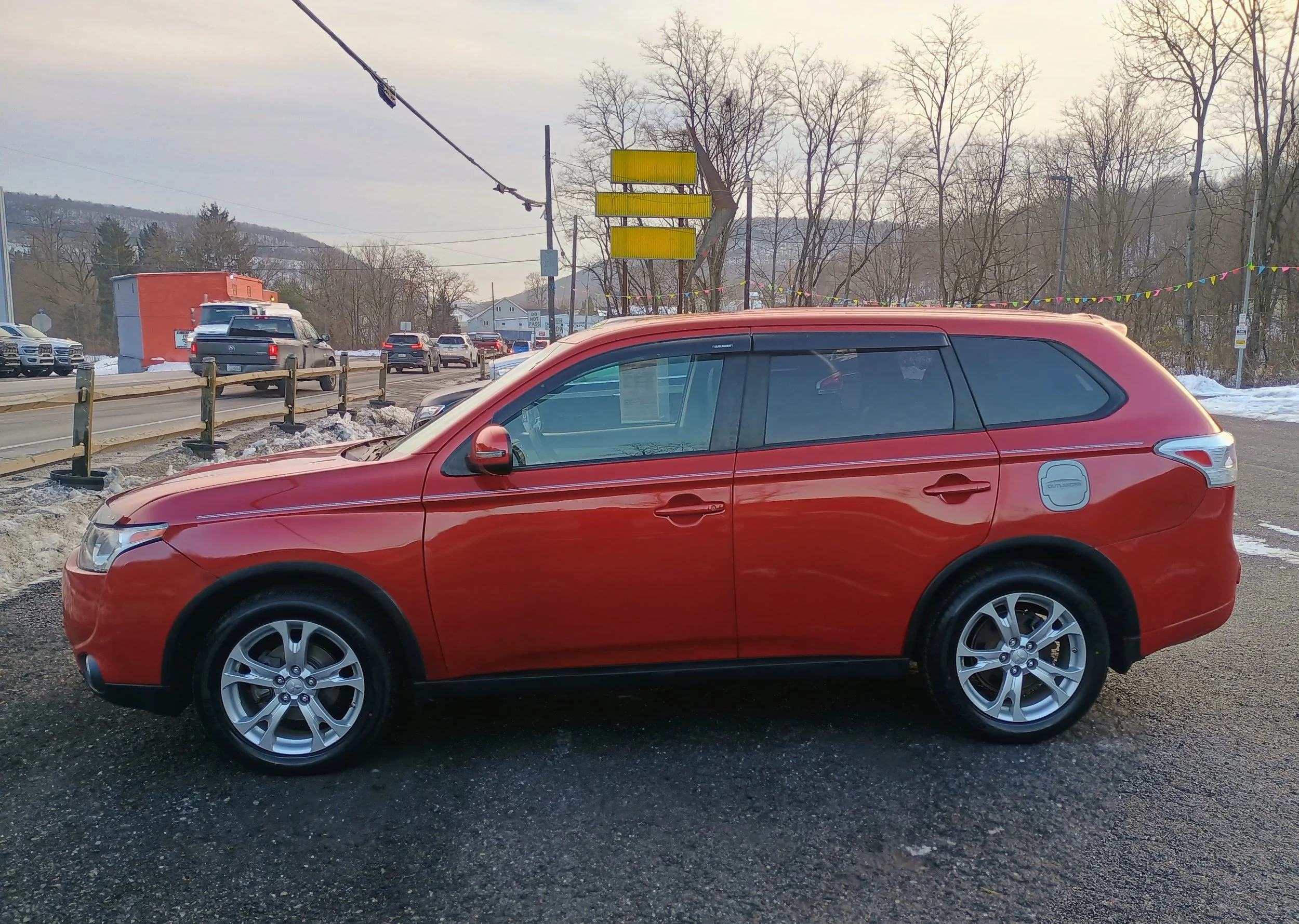 Red SUV parked on a parking lot with traffic and a snow-covered landscape in the background.