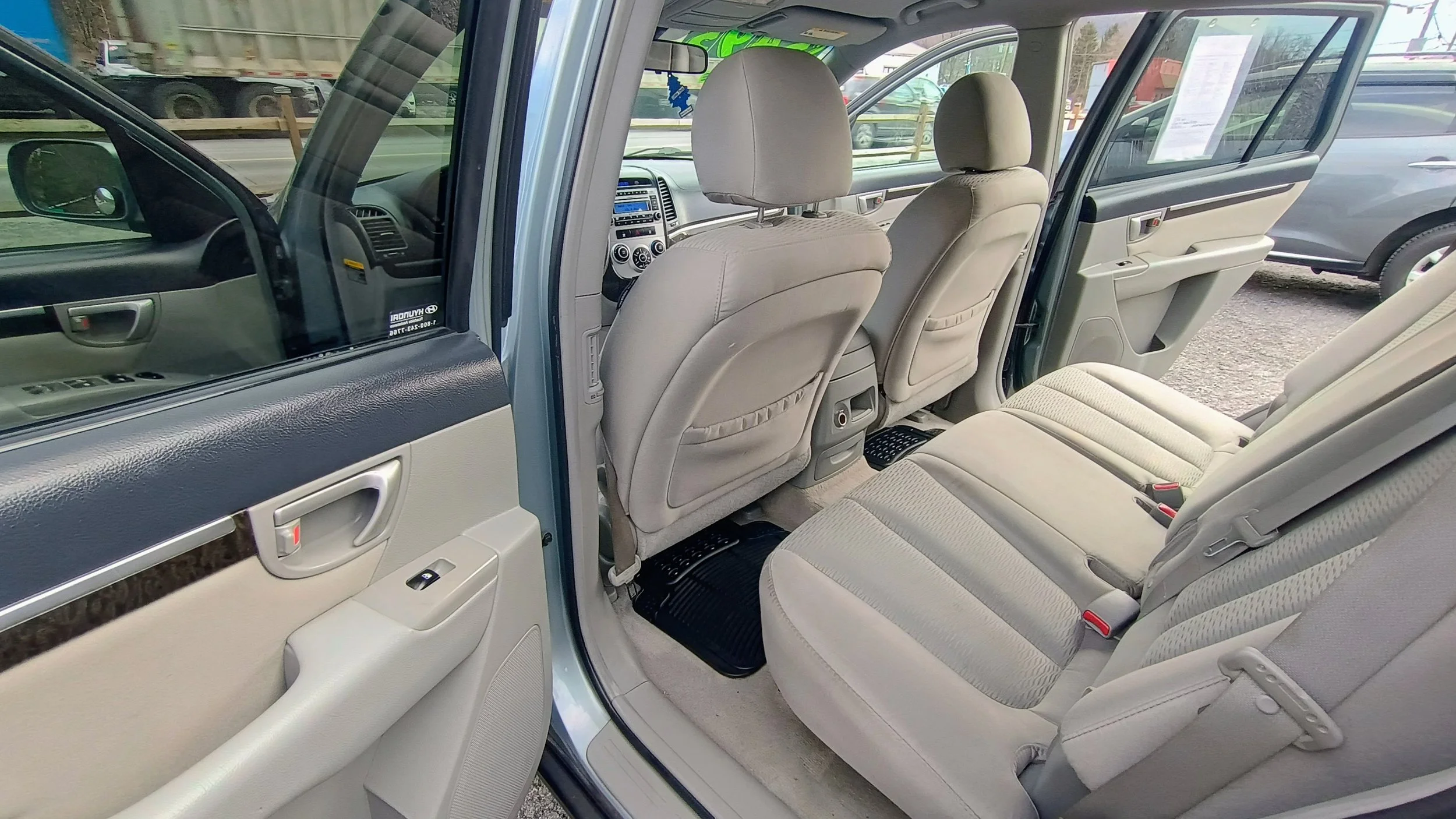Interior of a silver SUV showing the second row of beige fabric seats, beige door panels, and dashboard with a stereo system, with other vehicles parked outside.