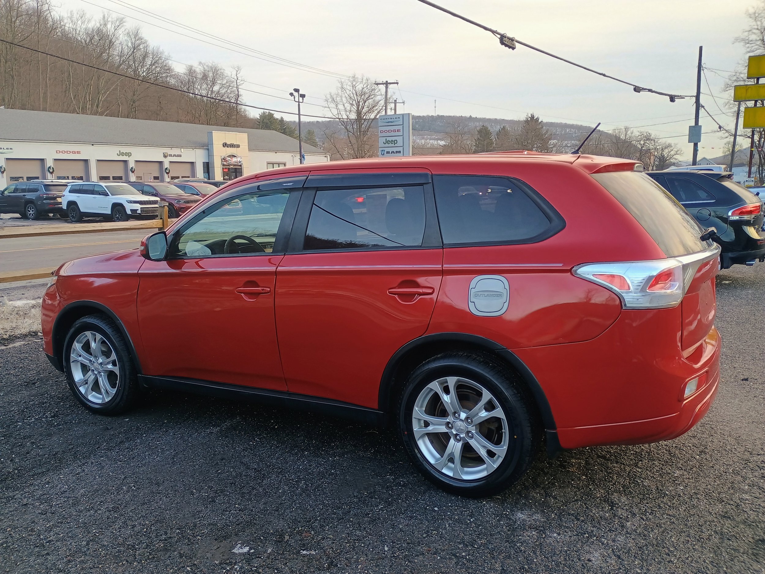 Red SUV parked in a lot outside a car dealership with other vehicles and a building in the background.