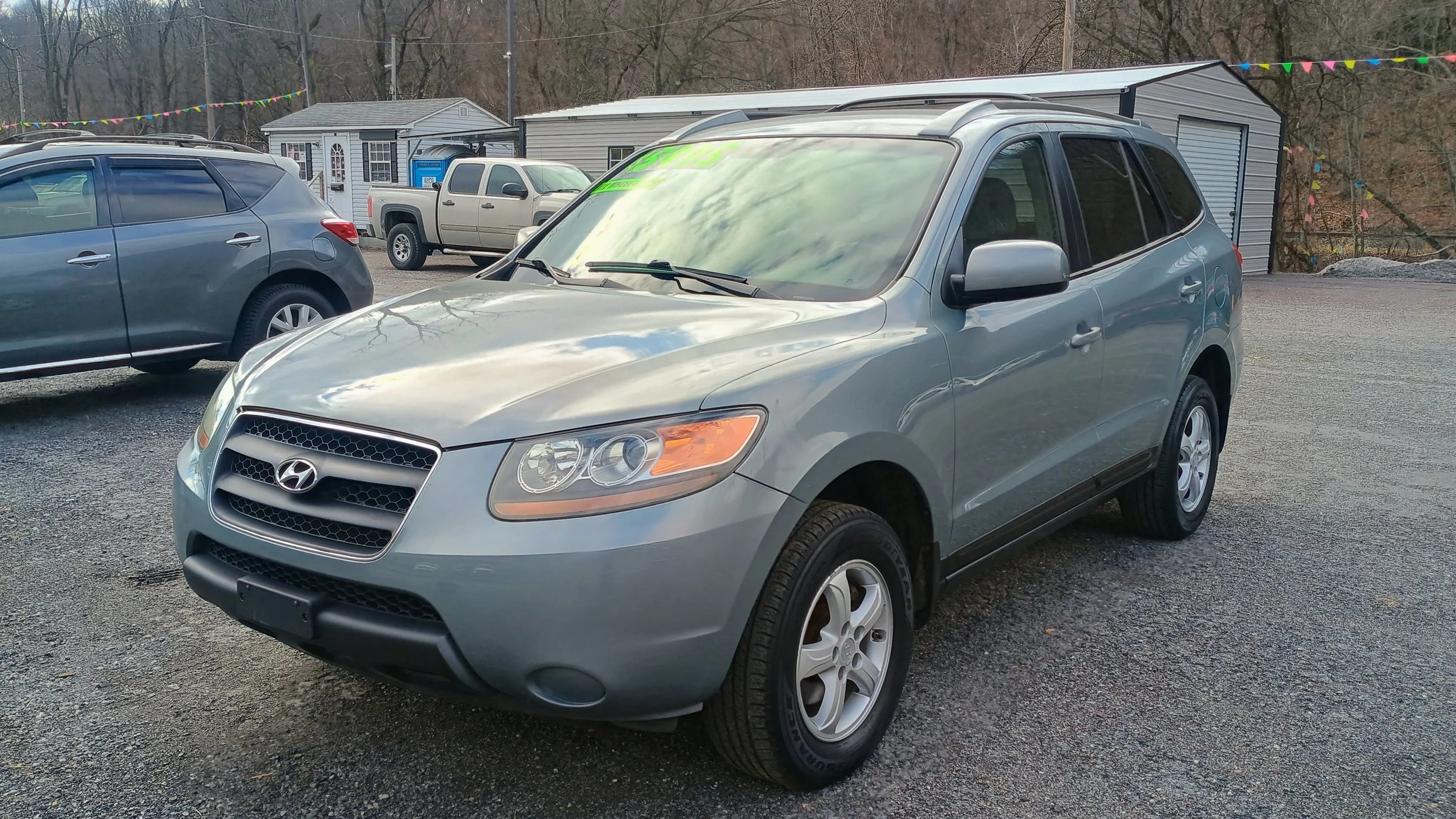 Silver Hyundai SUV parked in a gravel lot with other cars and a small building in the background, decorated with colorful pennant banners.