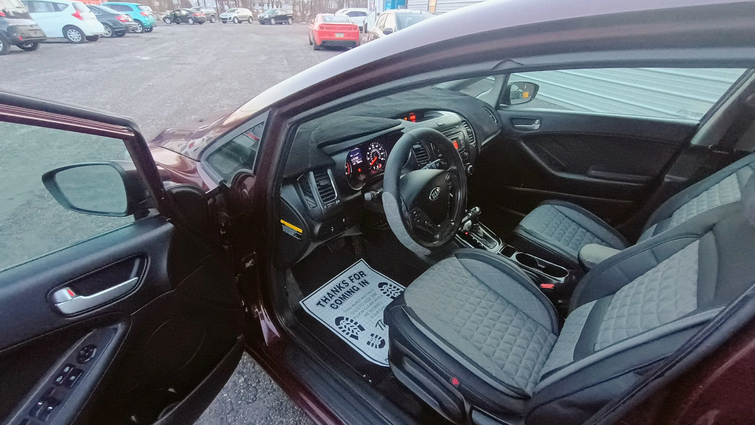 Interior of a car showing the dashboard, steering wheel, front seats, and driver's side door with window controls on a vehicle parked in a lot.