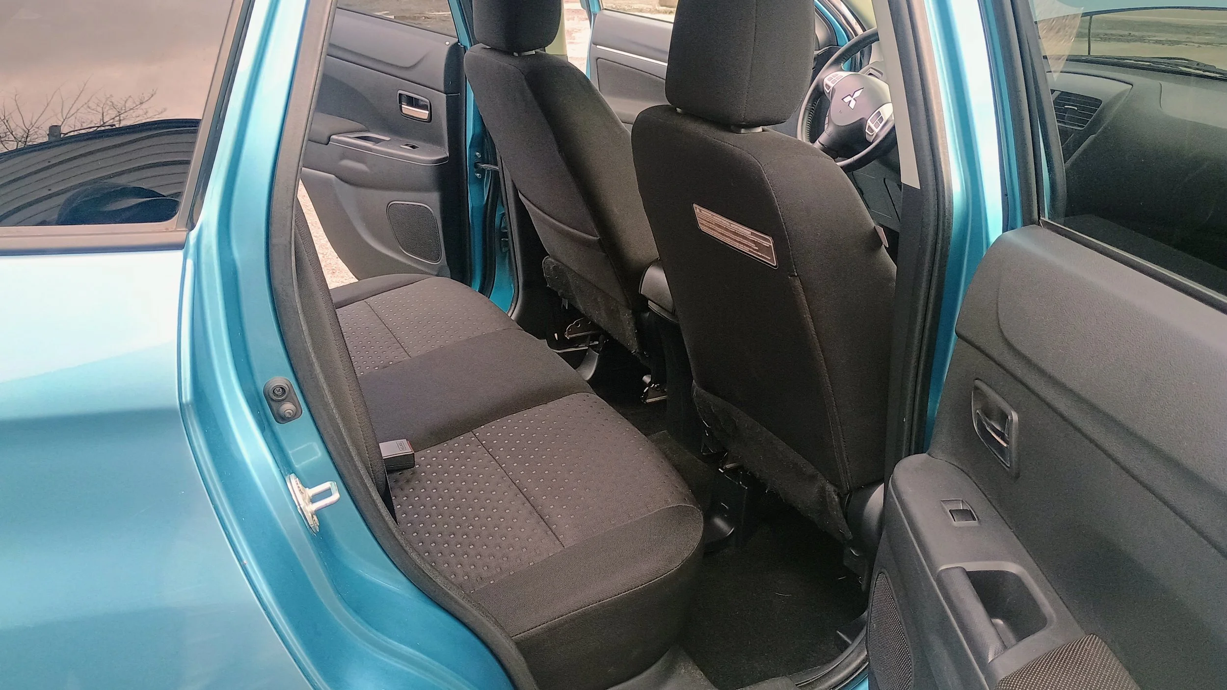 The interior of a blue compact car showing the back passenger seats, front seats, dashboard, and steering wheel.