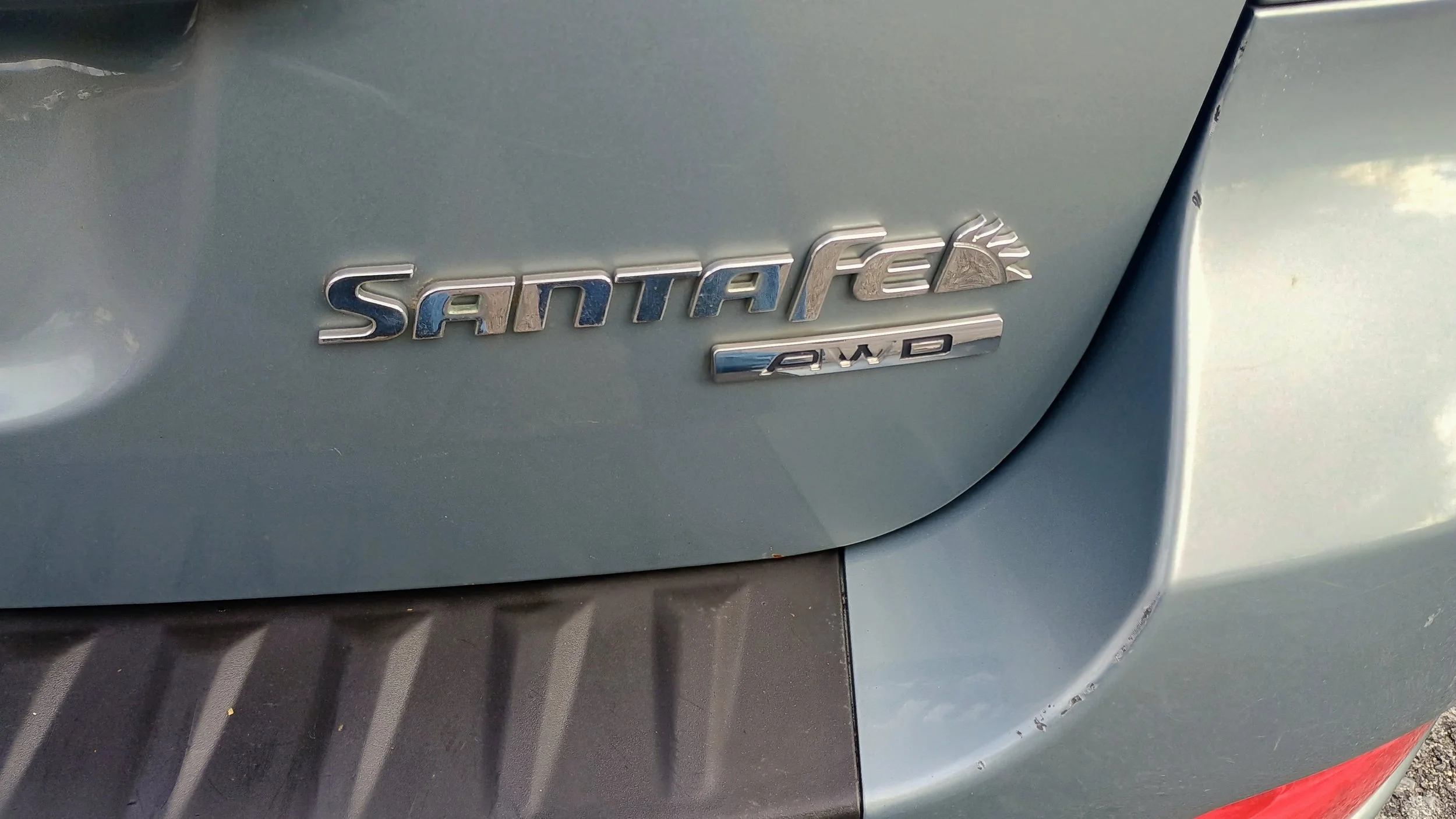 Close-up of a silver vehicle's rear badge reading 'SANTAFE' with a sun symbol and '2WD' below it.