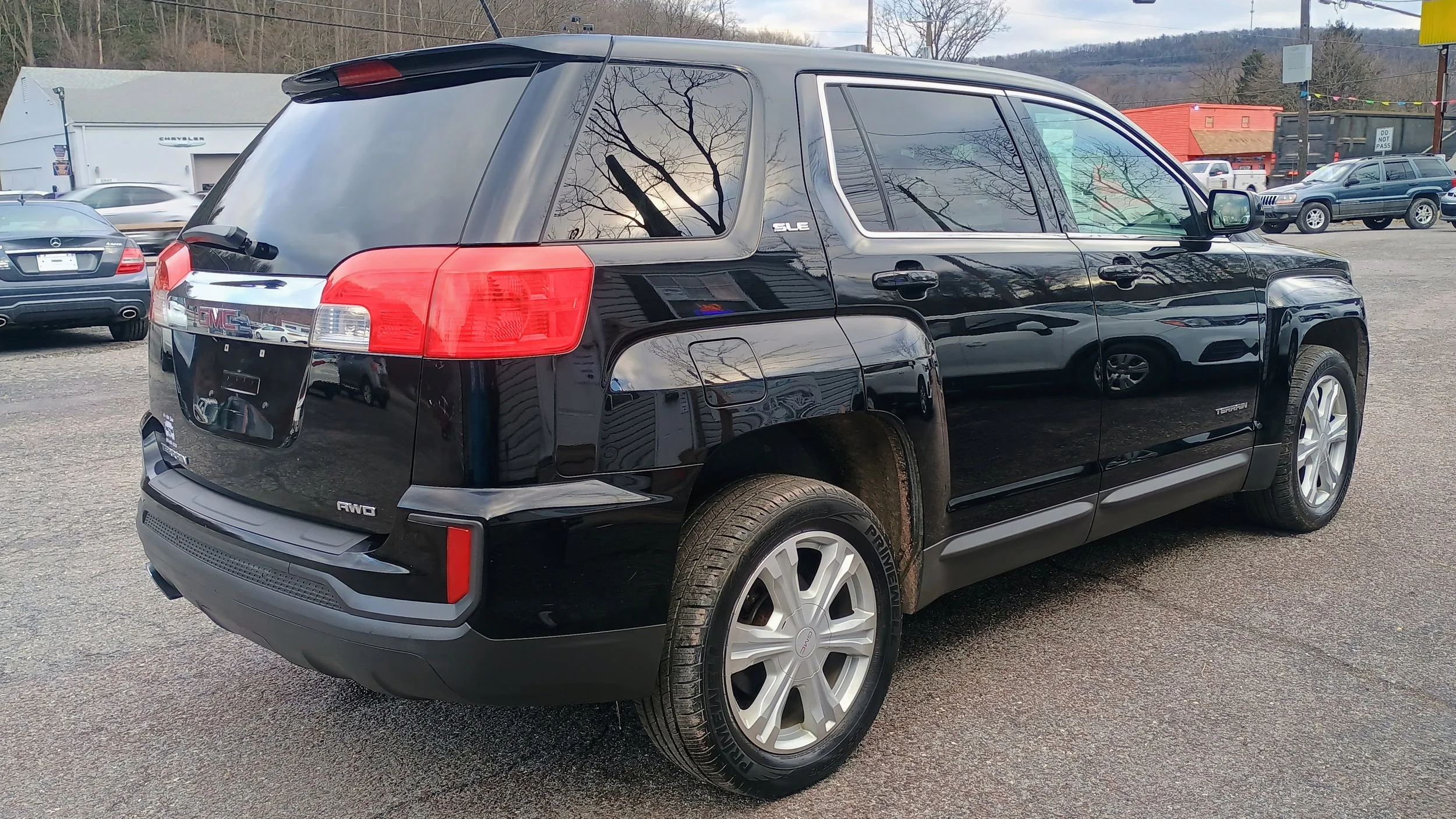Black GMC Terrain SUV parked in a lot with other vehicles, reflected trees and buildings in the windows.