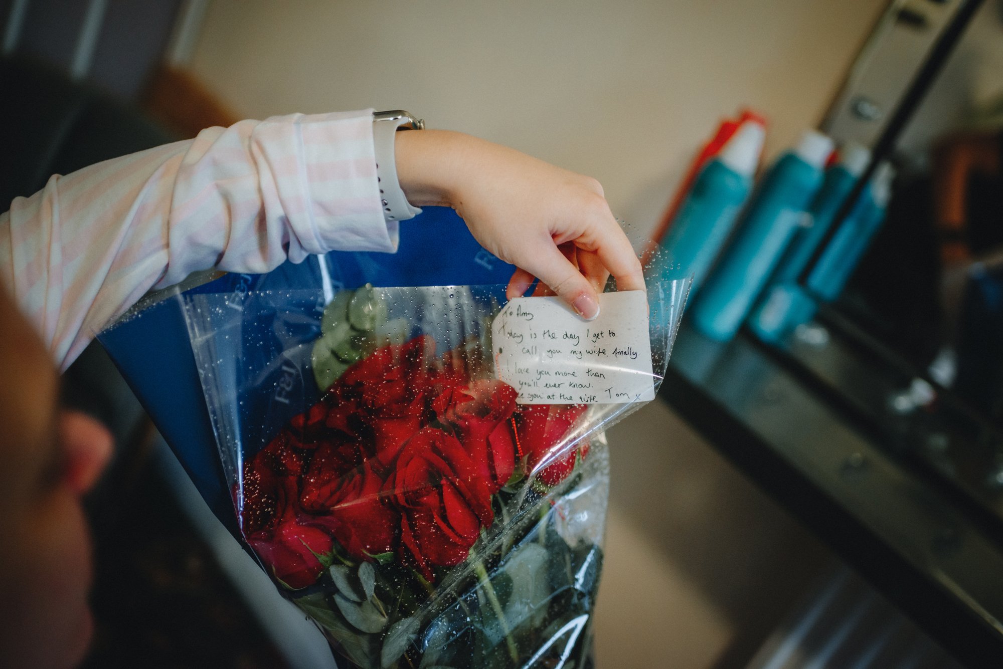 A person holding a bouquet of red roses with a handwritten note attached in a plastic wrap. The note is addressed to Amy, expressing love and affection.