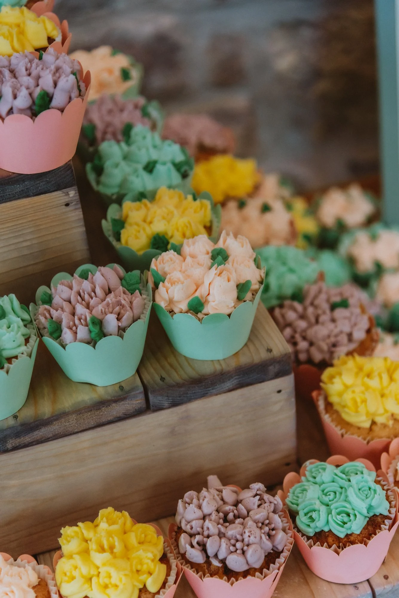 Colorful cupcakes with pastel frosting and sprinkles on a wooden display.