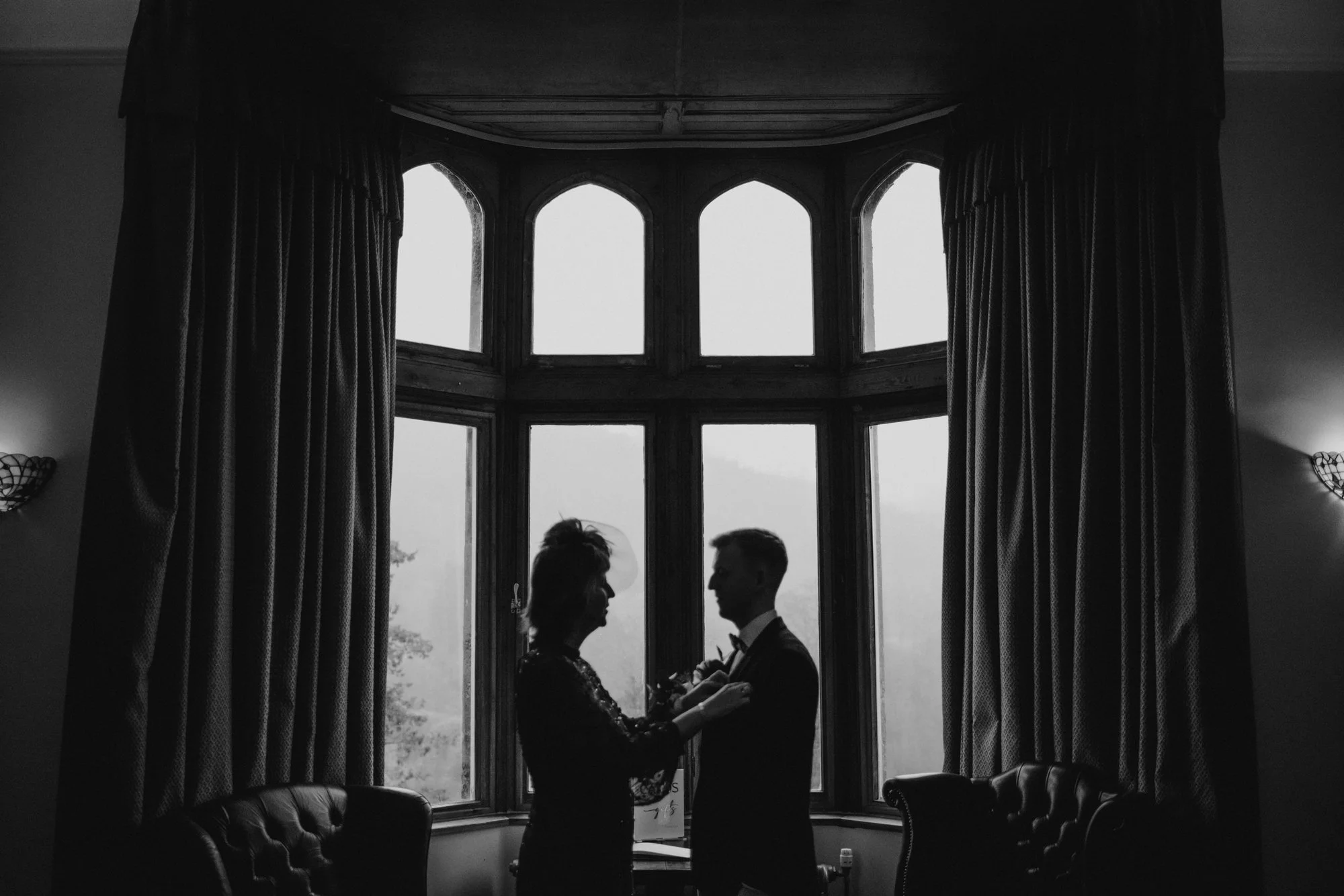 Silhouette of a couple standing in front of a large bay window, holding hands and facing each other indoors.