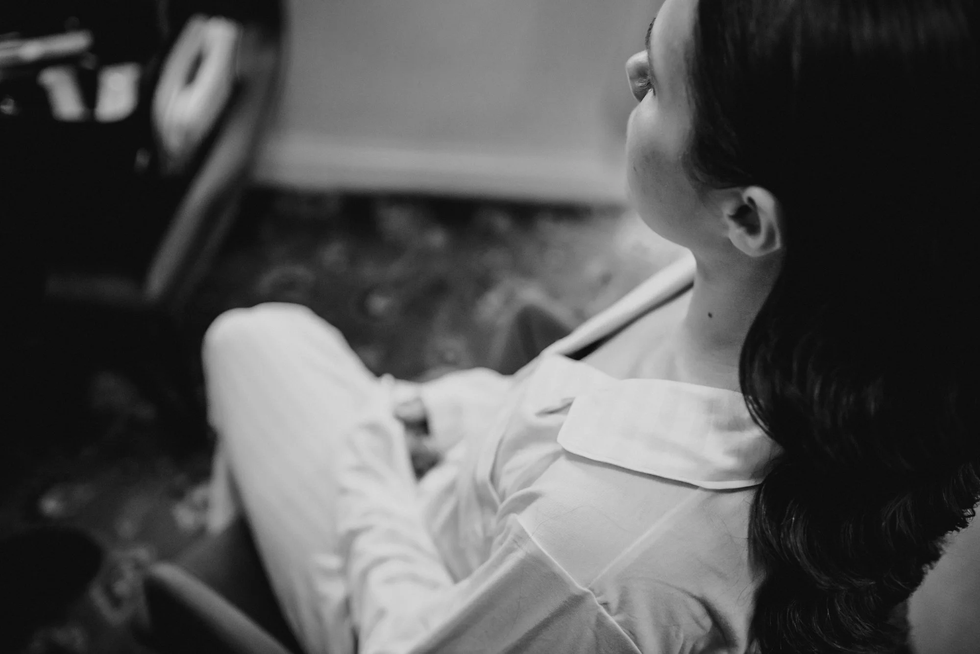 A woman with dark hair in a low ponytail, wearing a light-colored shirt, is sitting with her eyes closed in what appears to be a medical setting.