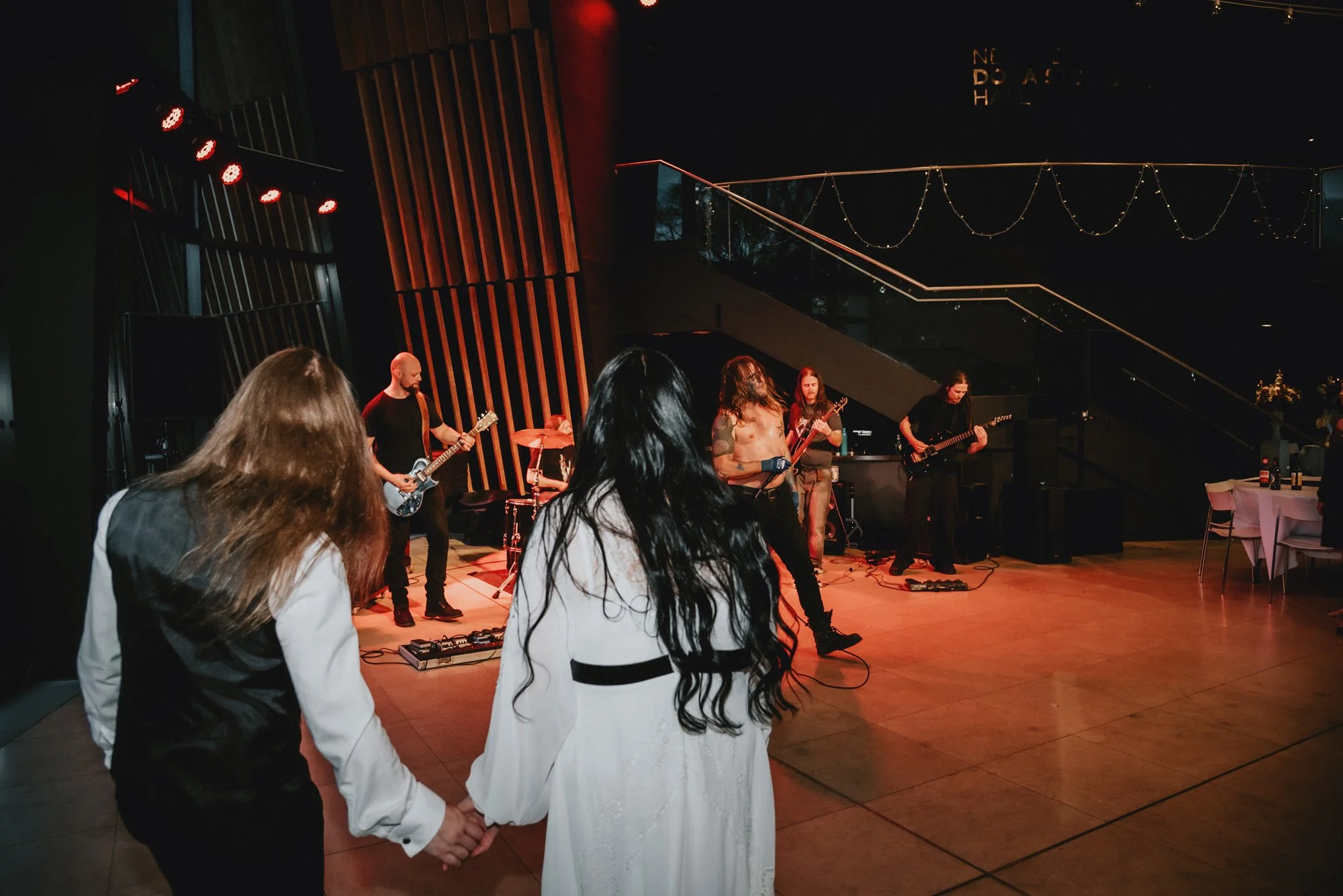 People dancing together while a band performs on stage at an indoor event.