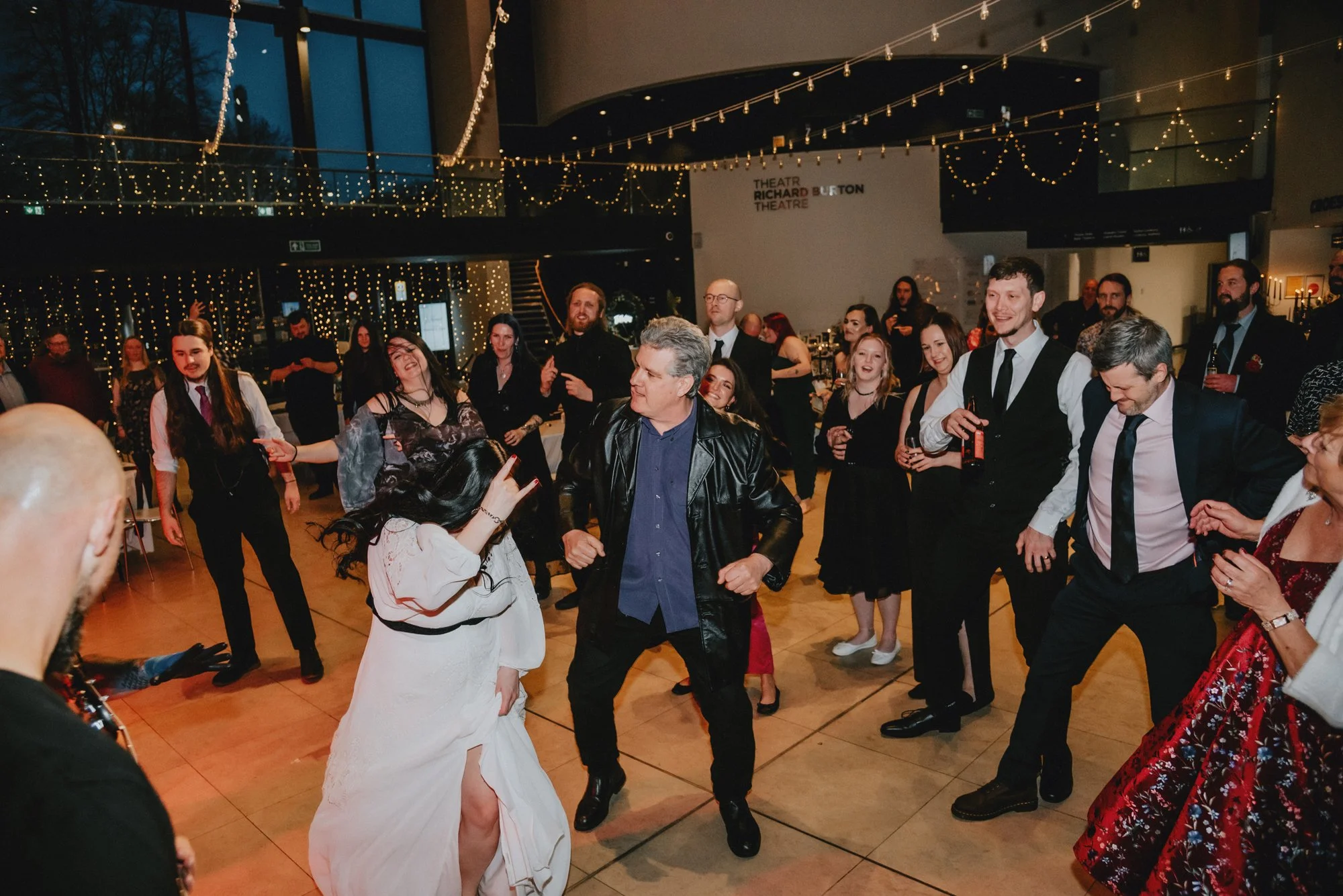 People dancing at a party or celebration in a decorated indoor venue with string lights.