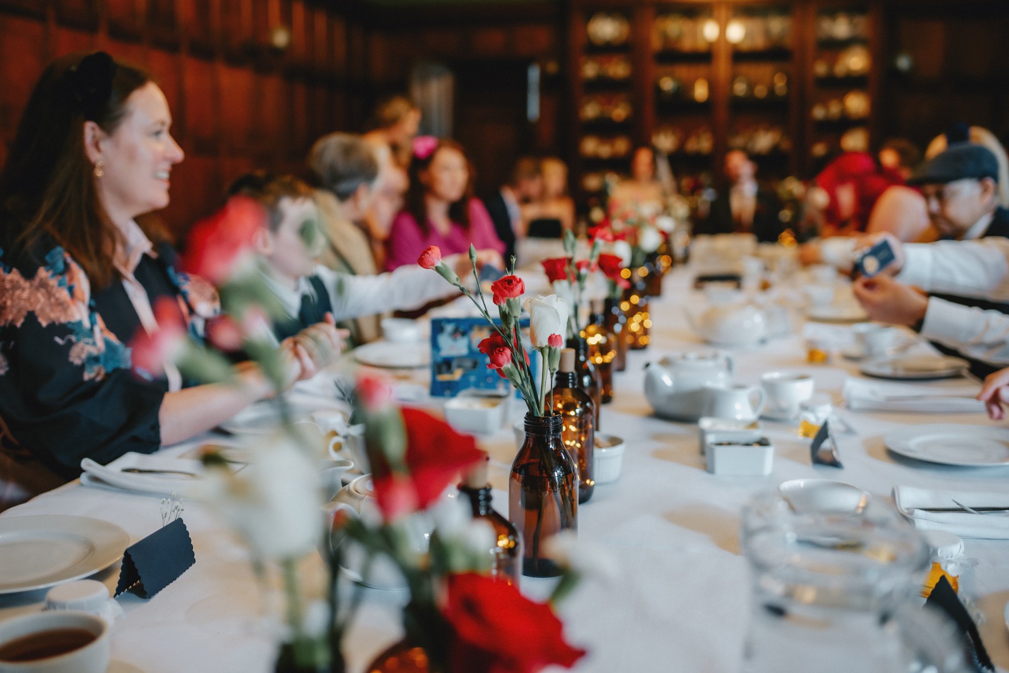 A family gathering at a long dining table with floral centerpieces and breakfast dishes in a wood-paneled room.