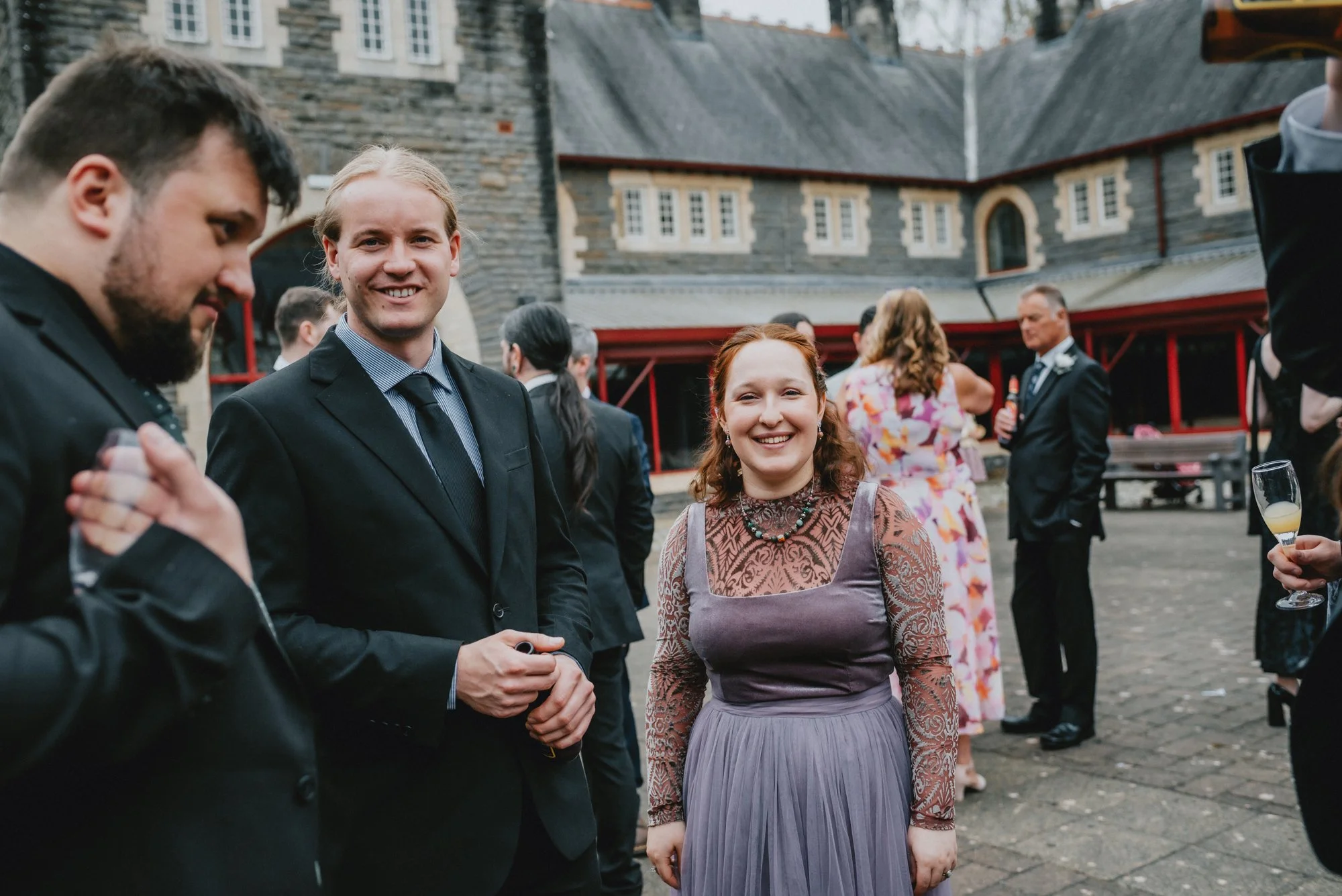 A group of people at a formal outdoor event, with a woman in a purple dress smiling at the camera.