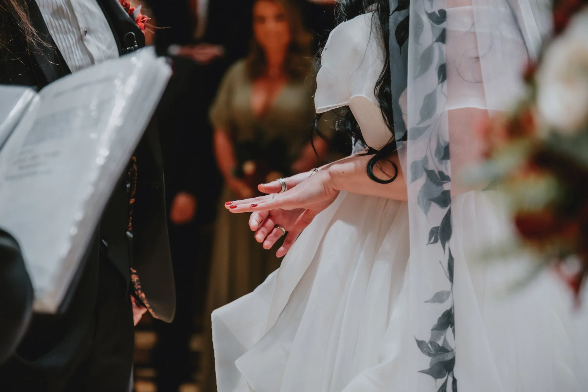 A bride wearing a white dress playing the piano during a wedding ceremony, with guests in the background.