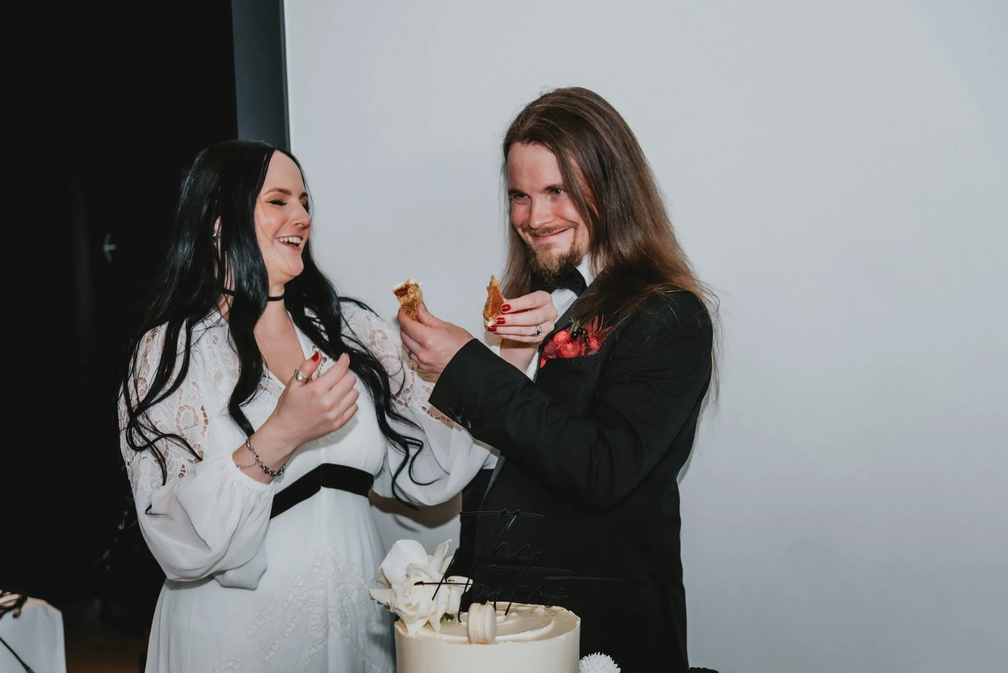 A man and woman in formal attire sharing a moment at a celebration, with a cake on the table.