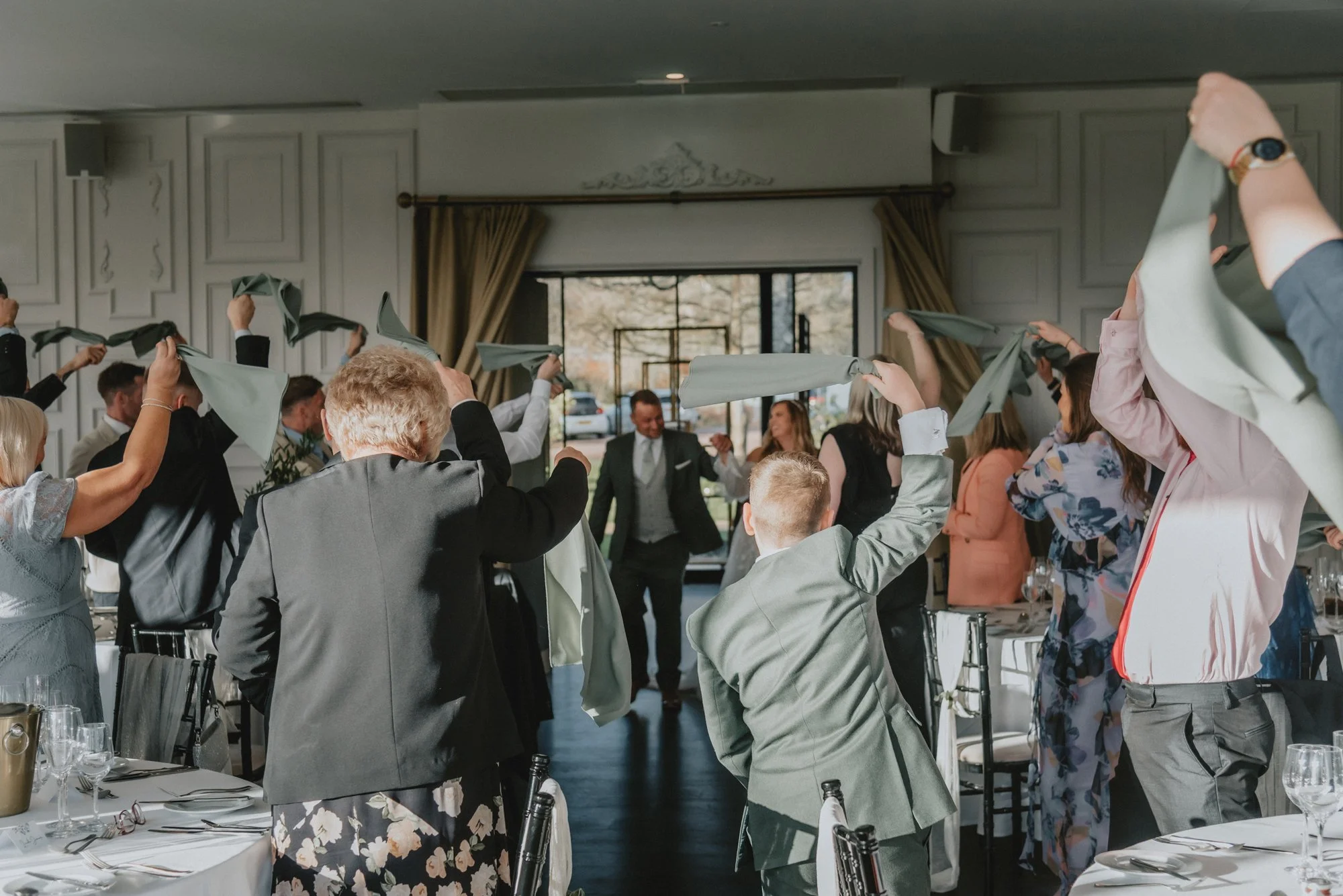 Guests at a wedding reception celebrating with a lively dance, waving cloth napkins in the air inside a decorated banquet hall.