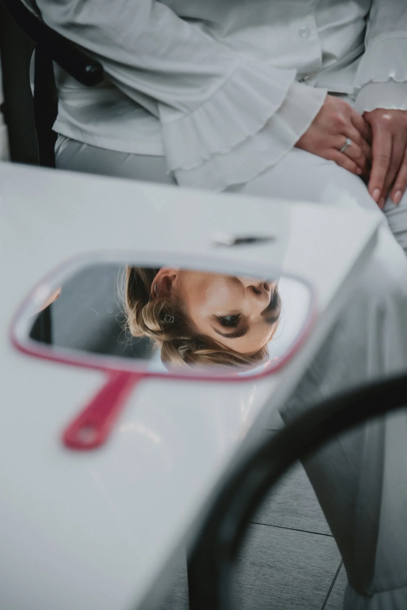 A woman looking at her reflection in the mirror with a dental tool. She has blonde hair and appears to be at the dentist's office.