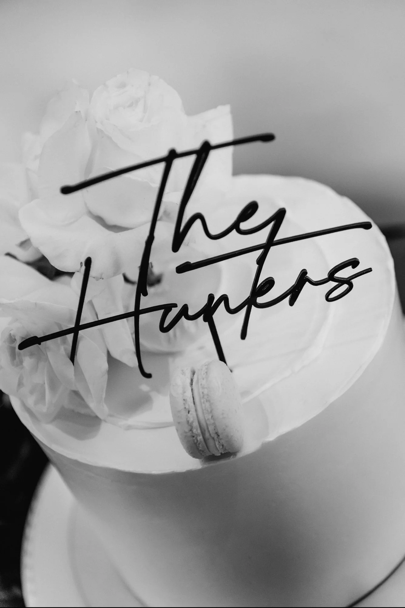 Decorative cake with a sign that says 'They Fought', flowers, and a macaroon on top in black and white.