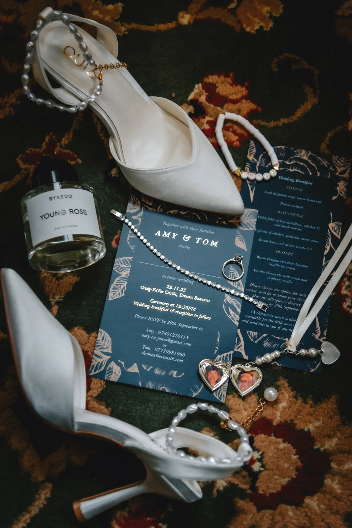 A pair of white high-heeled shoes, pearl jewelry, a wedding invitation for Amy and Tom, a bottle of perfume labeled 'Young Rose,' and various accessories are arranged on a patterned rug.