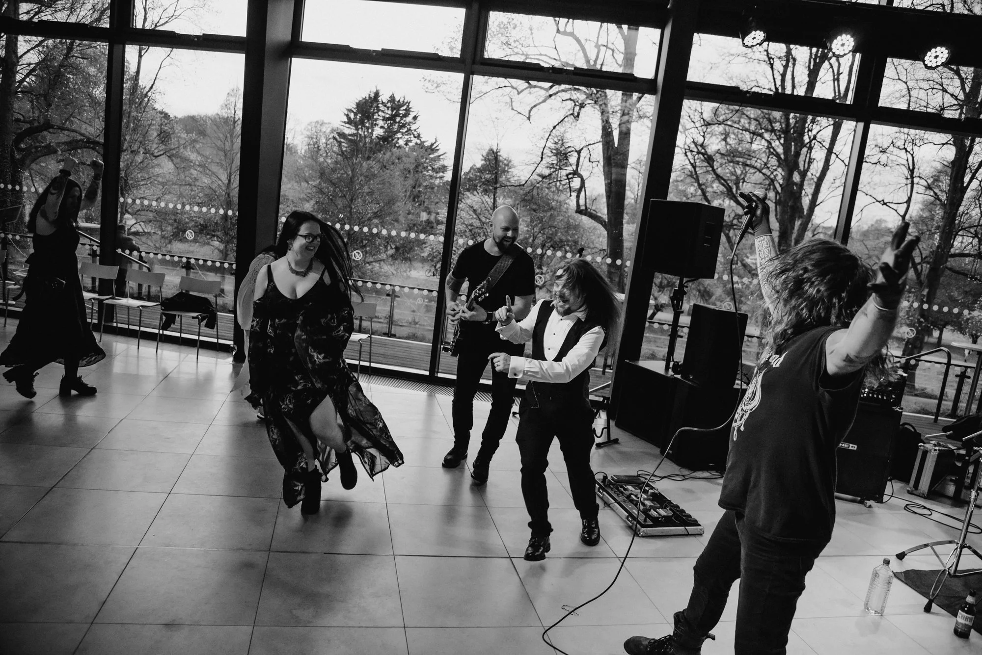 Musicians and dancers enjoying a lively performance in a bright indoor space with large windows showing trees outside