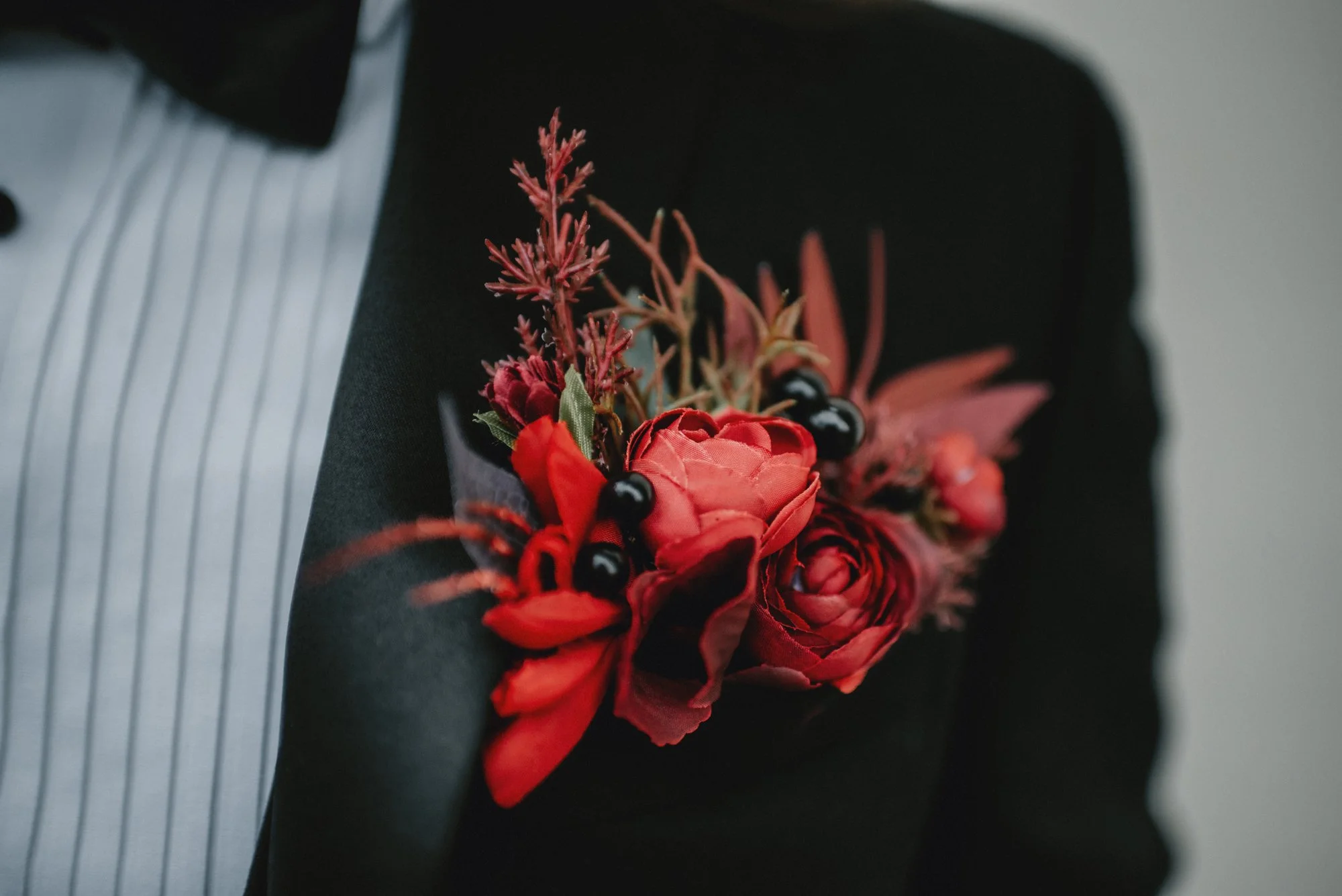 A person wearing a corsage with red and black flowers and greenery on their suit.