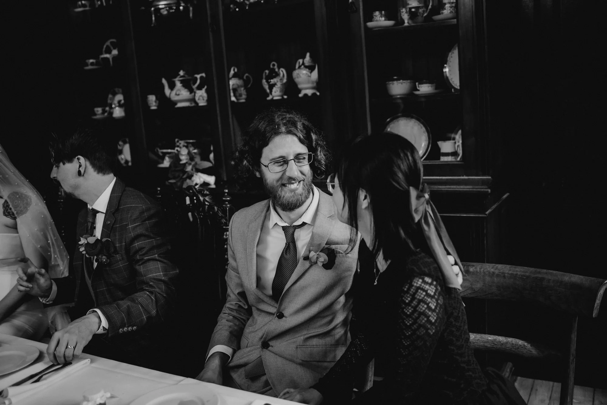A black-and-white photo of people sitting at a formal dinner, with a man in a light-colored suit and a woman in a dark dress engaged in conversation.
