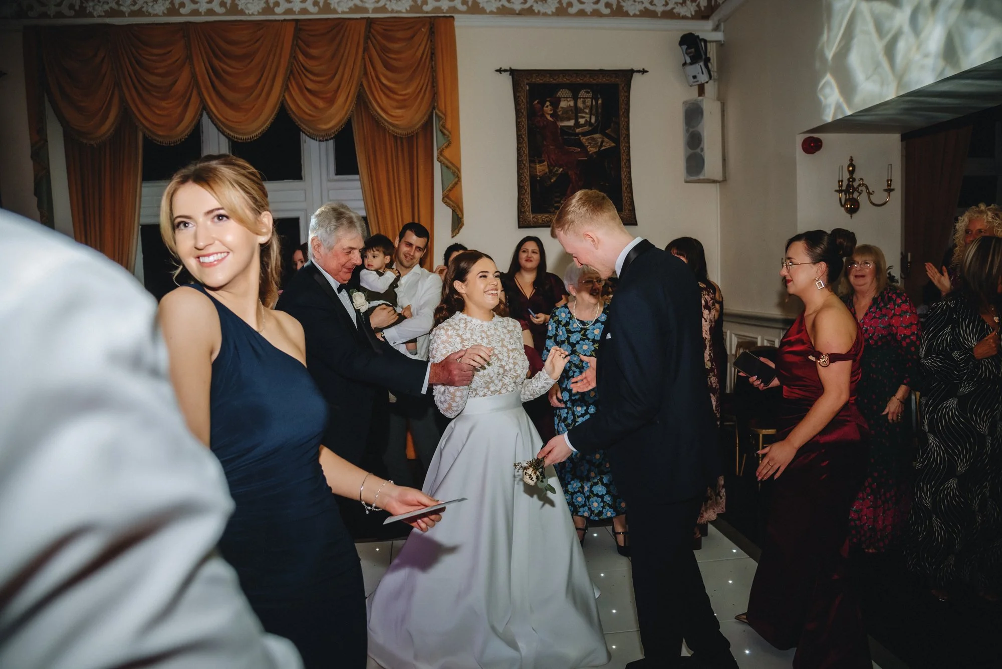 People dancing and celebrating at a wedding reception inside a decorated hall.