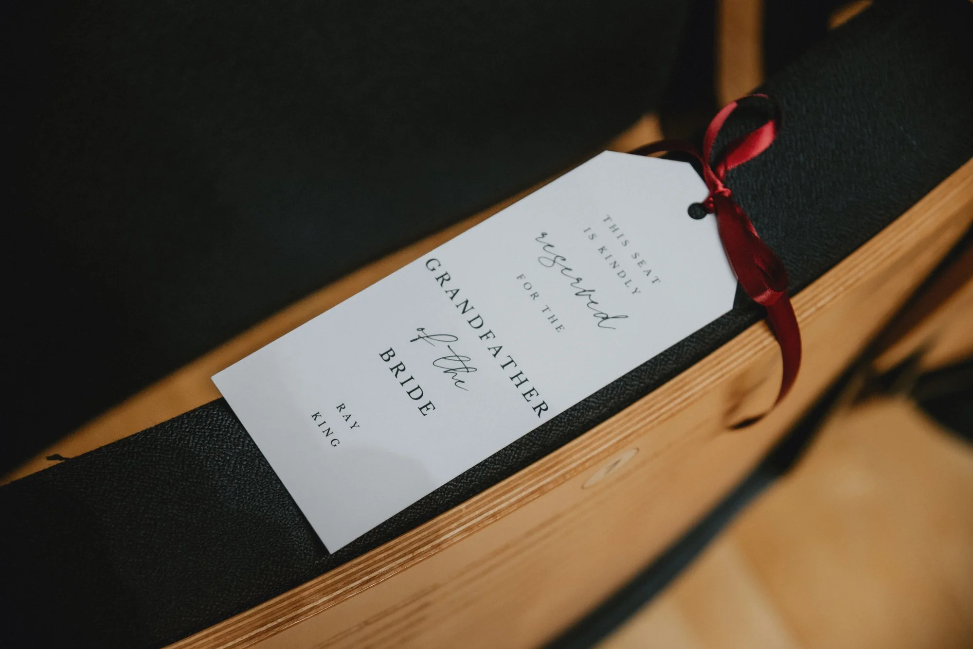 A black and wooden bench with a white wedding program tied with a red ribbon on top.