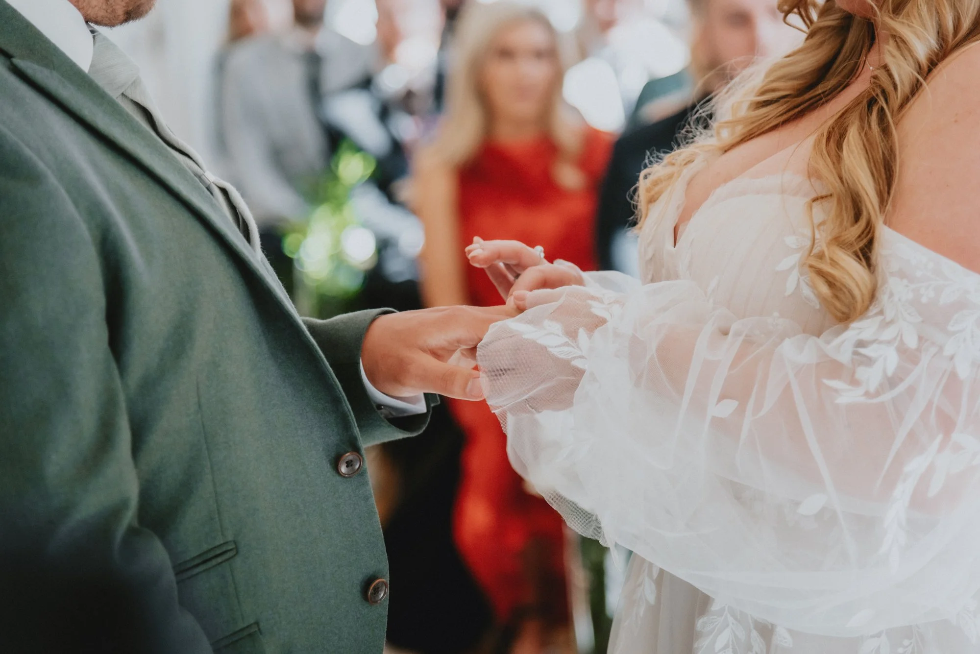 Close-up of a couple exchanging wedding rings during a ceremony, with guests in the background.