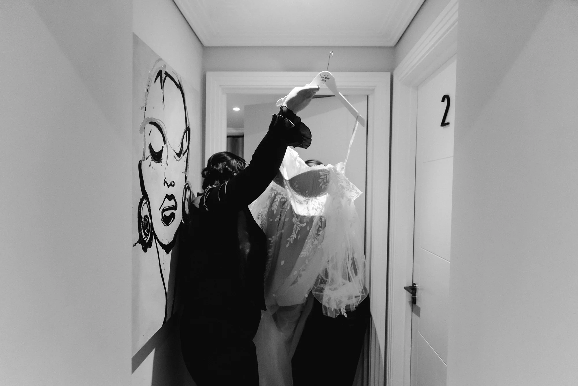 A person with vintage hairstyle hanging a wedding dress on a hanger inside a house.