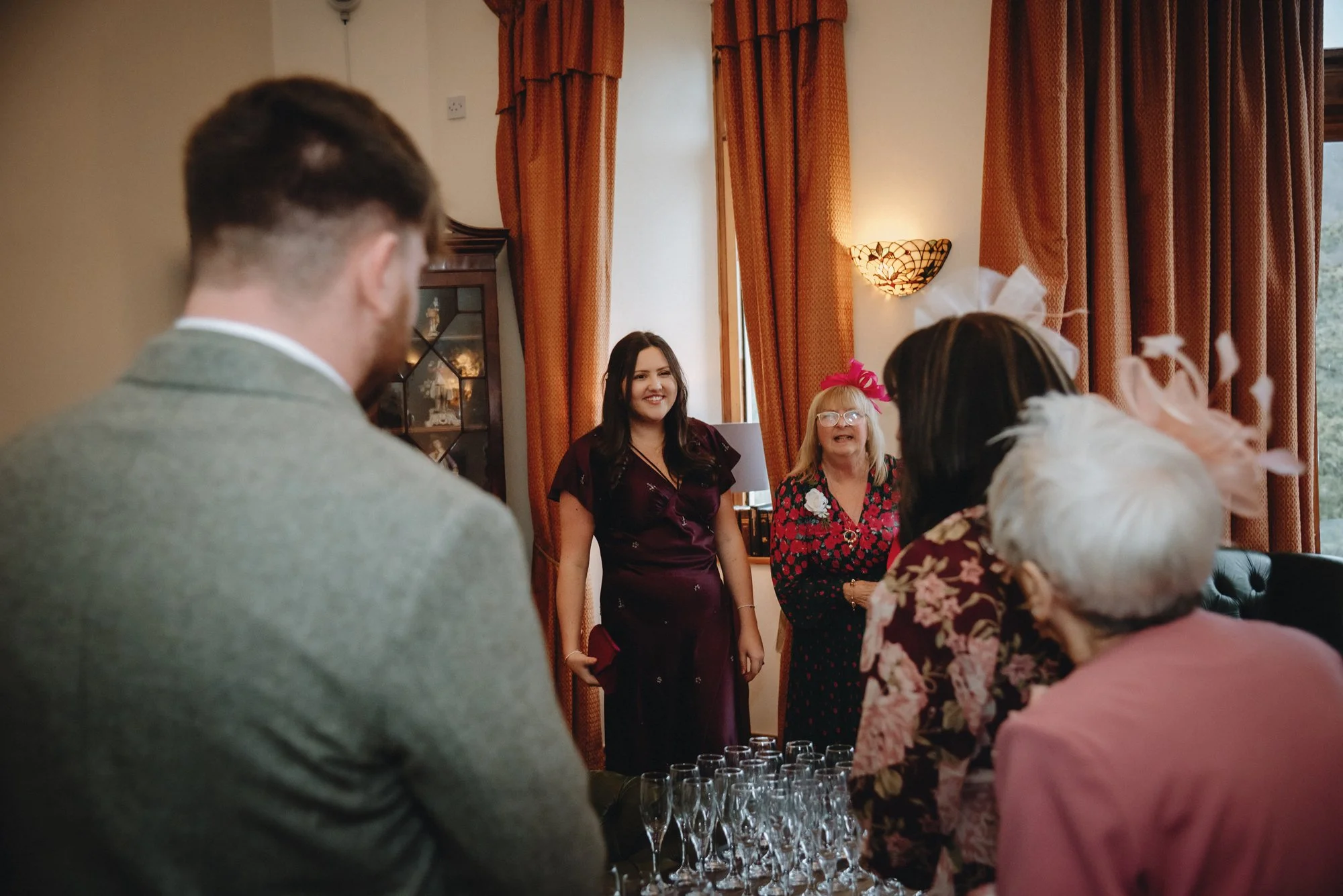 A group of people celebrating indoors, with women in the background smiling, and a man and woman in the foreground looking at each other, near a table with champagne glasses.