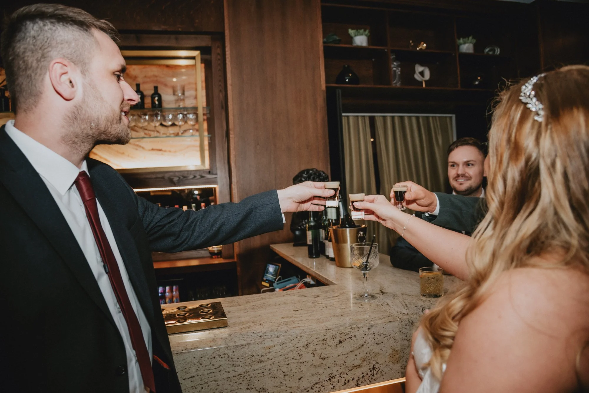 A group of people celebrating at a bar, toasting with shots of dark liquor.
