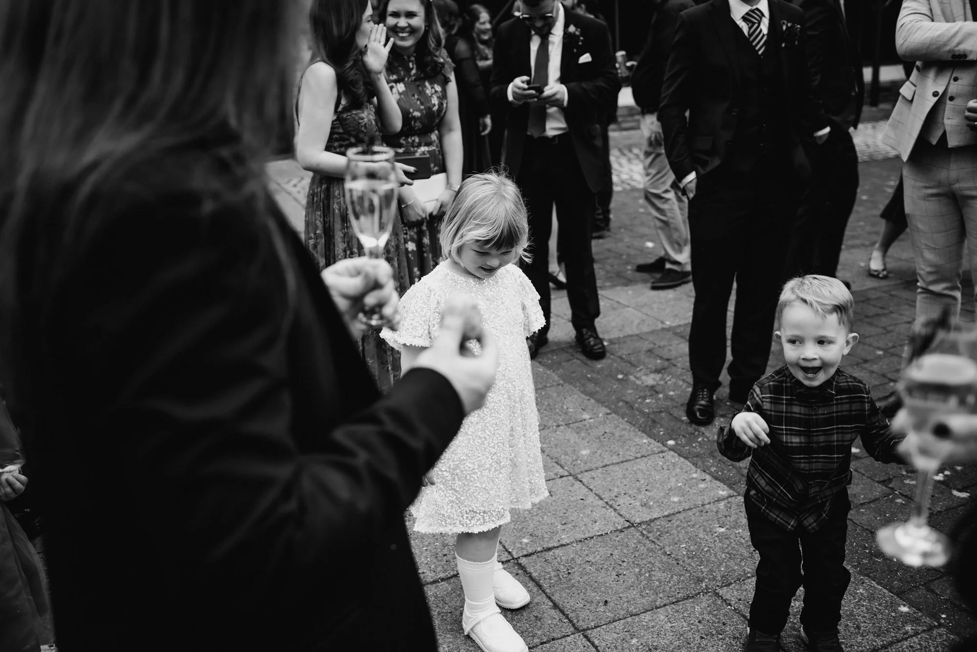 Children dancing at an outdoor celebration with adults holding champagne glasses around them.