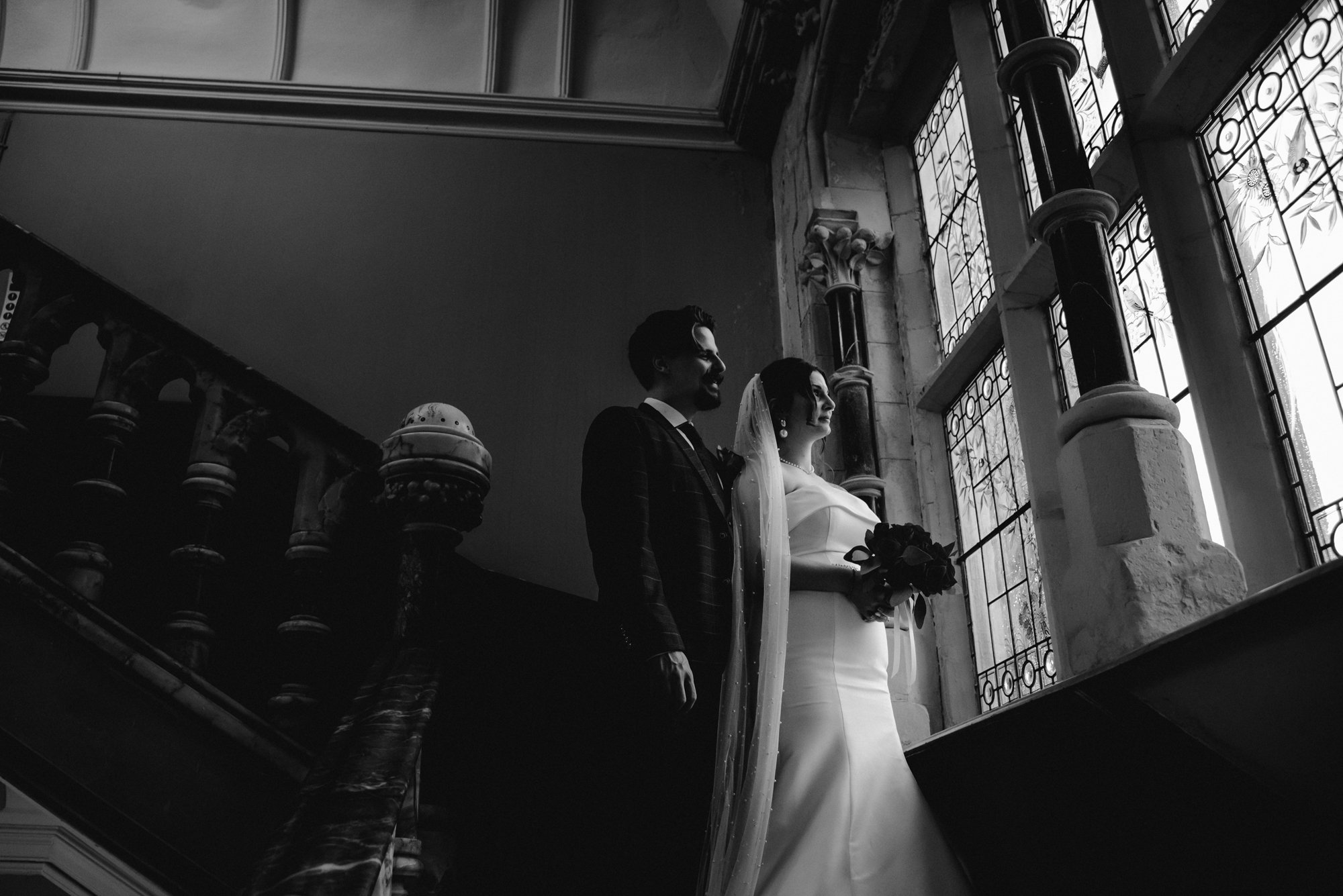 A bride and groom standing together in a historic building with stained glass windows, black and white photo.