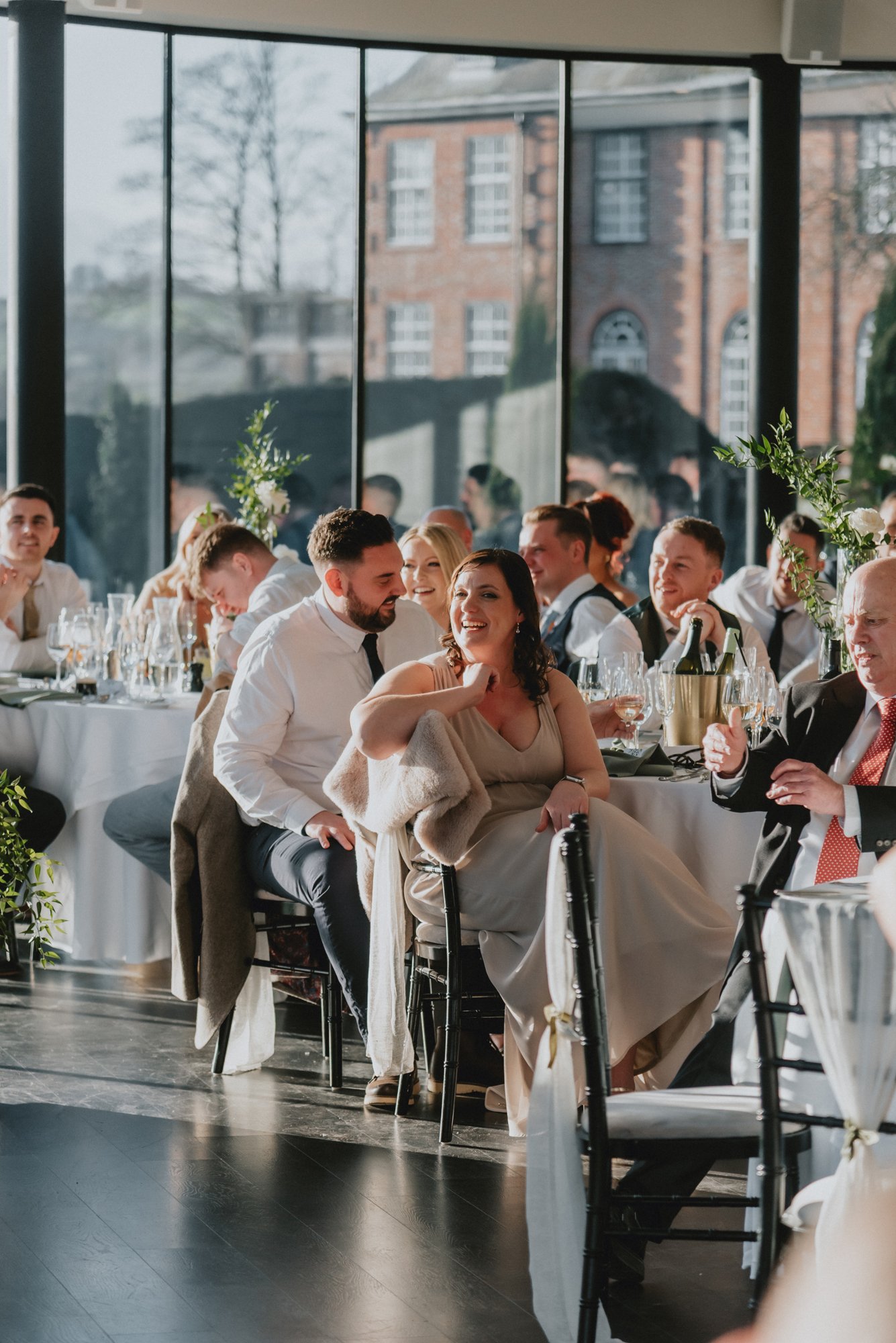 People celebrating at a formal gathering in a bright, elegant room with large windows and a view of old brick buildings outside.