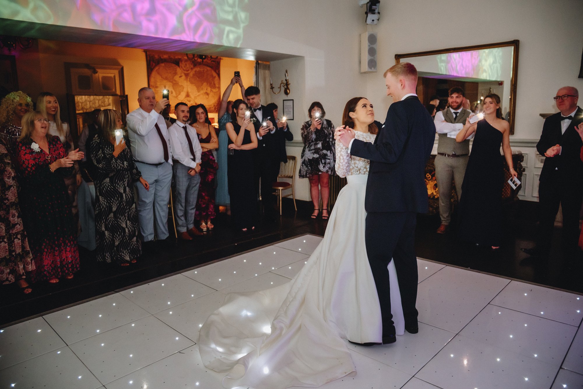 Bride and groom dancing at their wedding reception with guests watching and taking photos.
