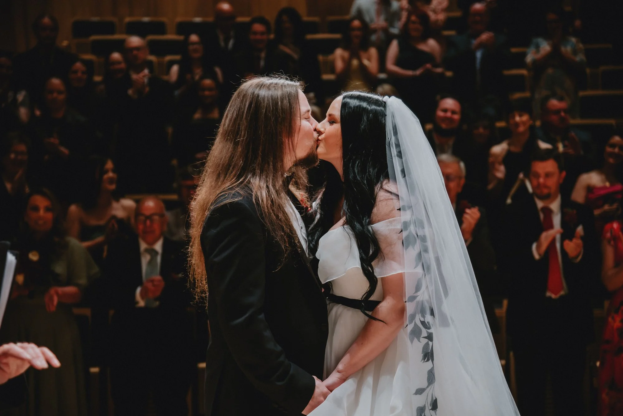 A couple kisses during their wedding ceremony in front of an audience.