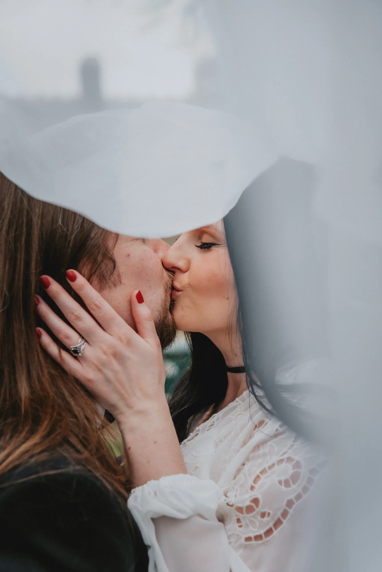 A couple kissing outdoors, partially obscured by a white balloon in the foreground.