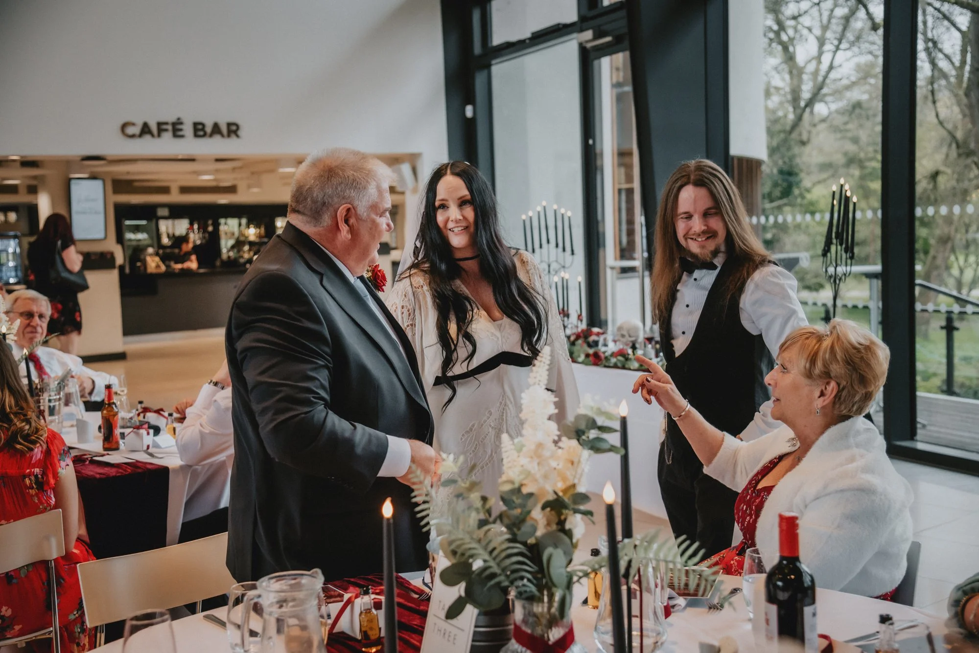 People at a decorated dining table in a modern restaurant, engaged in conversation, with large windows showing trees outside.