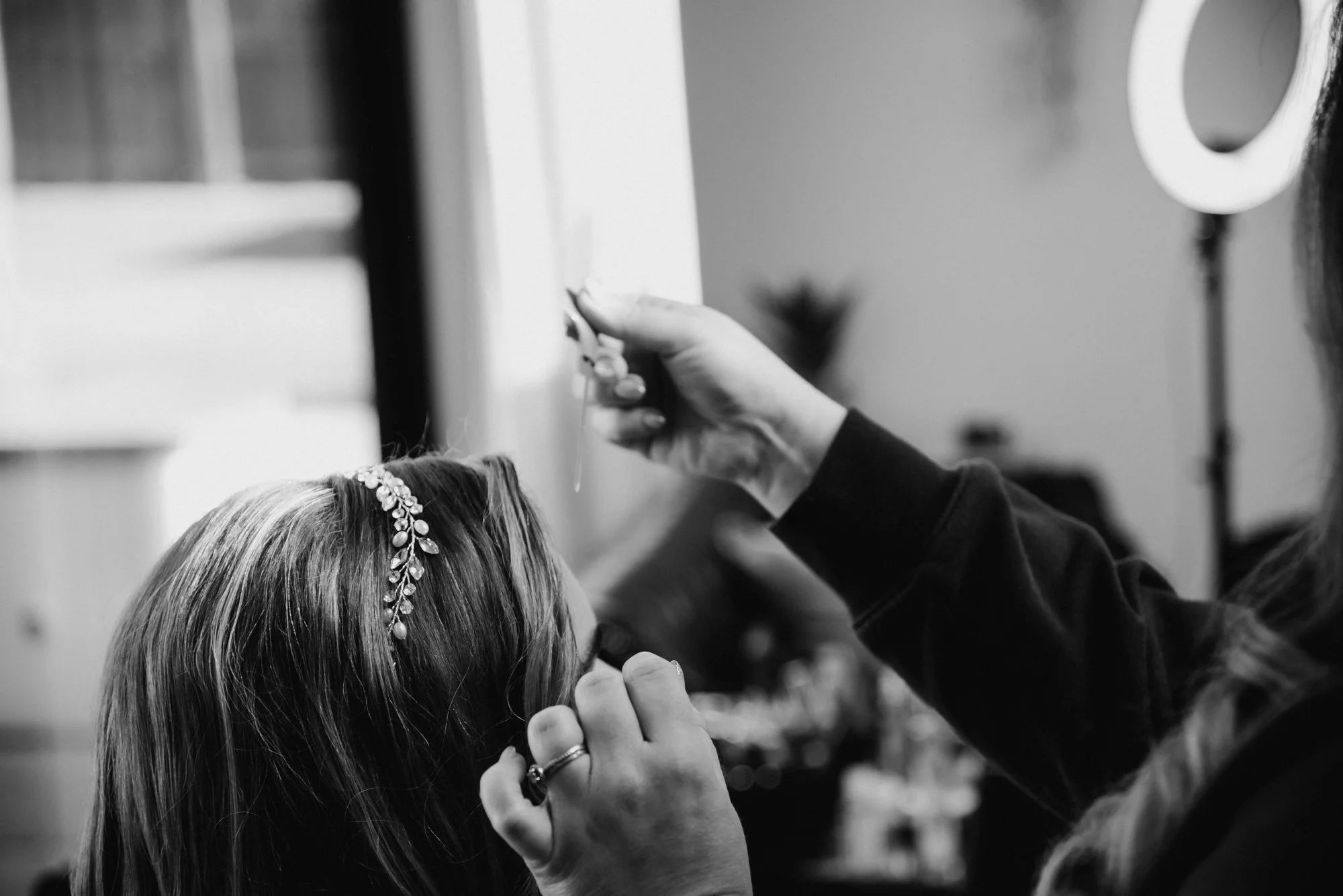 Makeup artist or stylist applying makeup or face paint to a woman with long hair and a floral headband in a salon or studio.