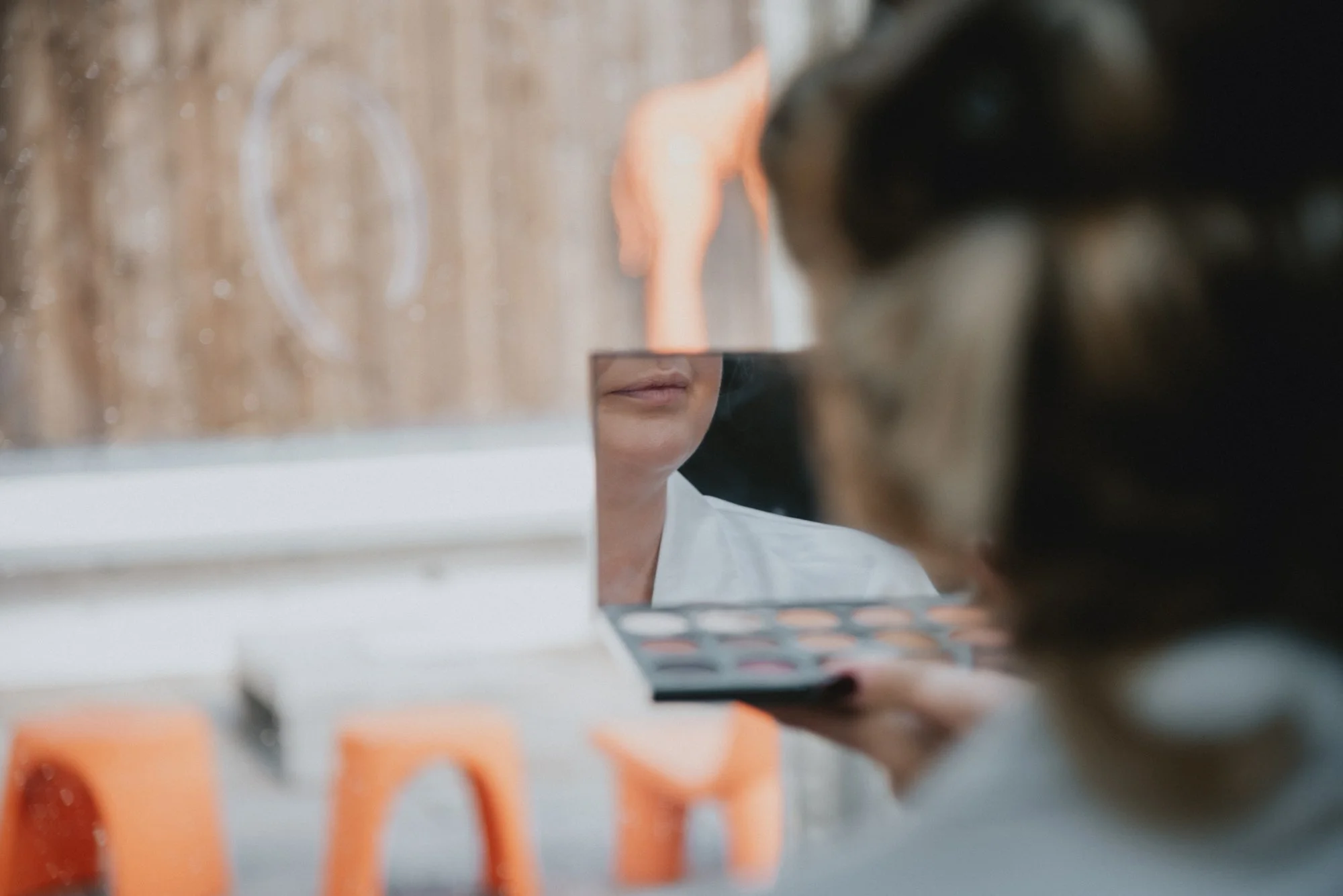 A woman applying makeup in front of a mirror, with makeup palettes and brushes in view.