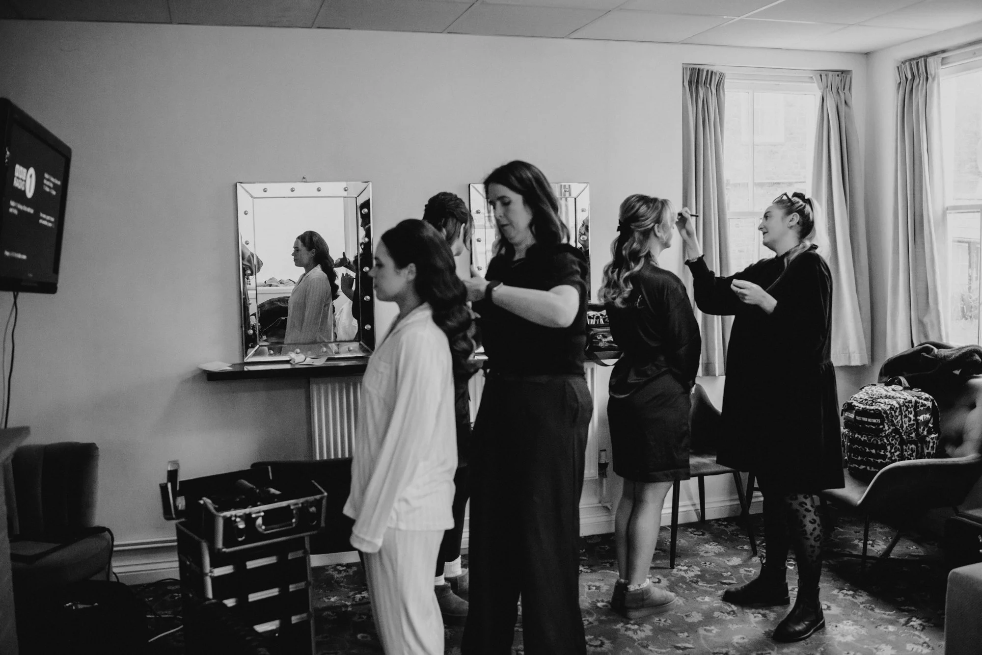 Women preparing for a fashion show in a dressing room, applying makeup and styling hair.
