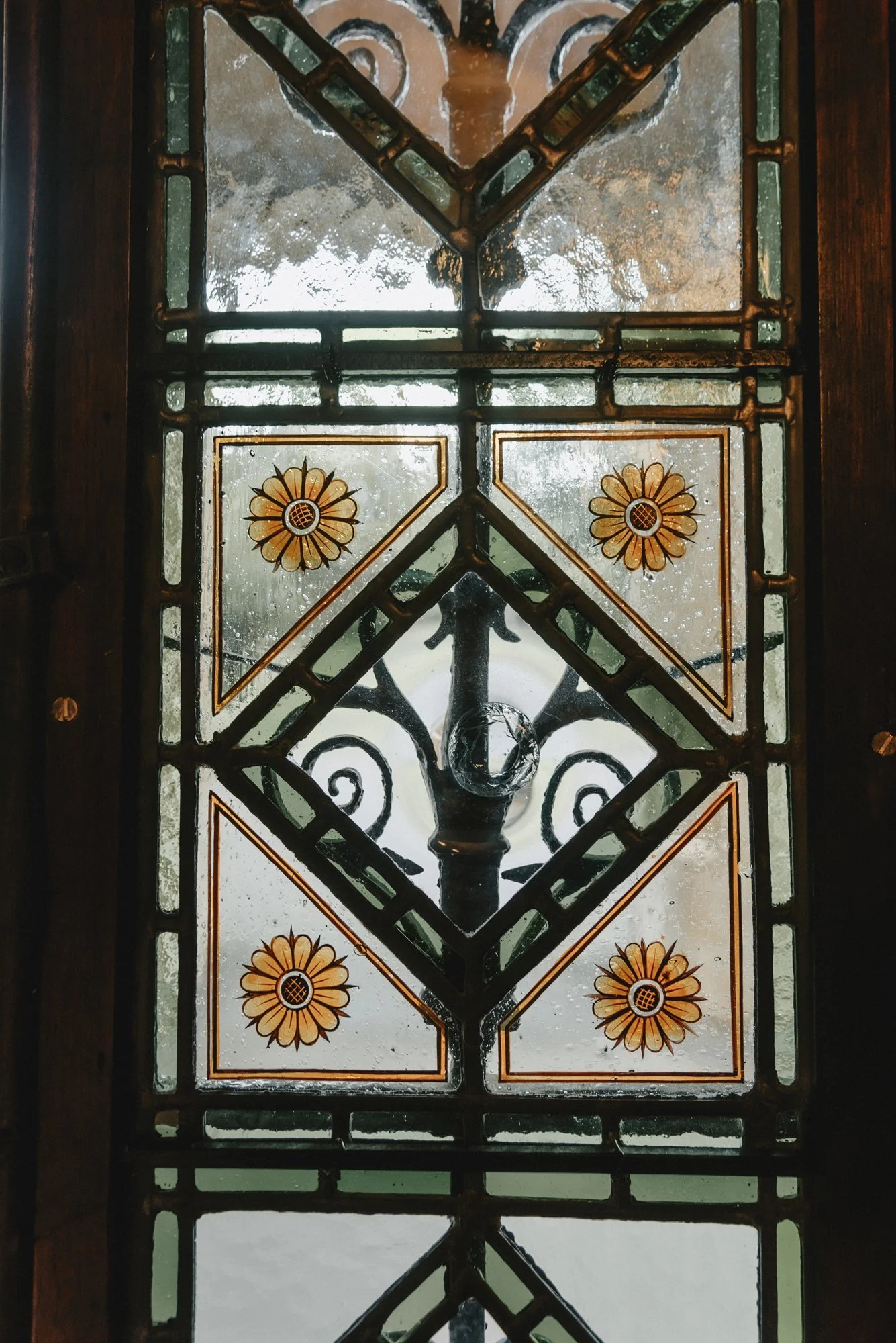 Decorative stained glass window with a metal frame, featuring floral designs and geometric patterns.