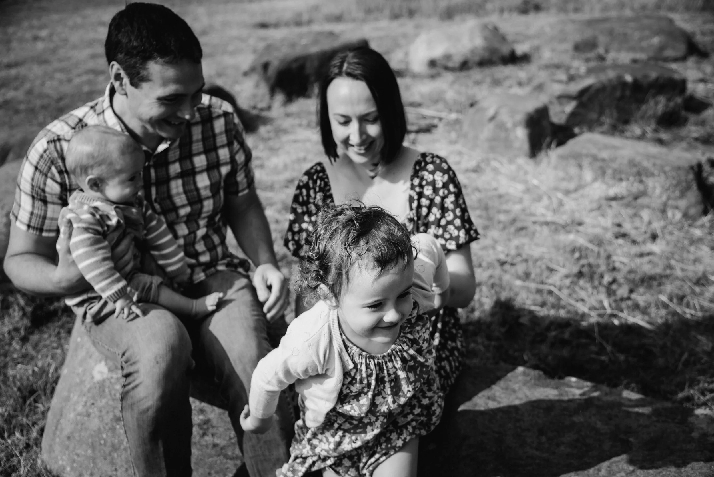 A black and white photo of a group of children and two adults outdoors on a grassy area, smiling and interacting with each other.