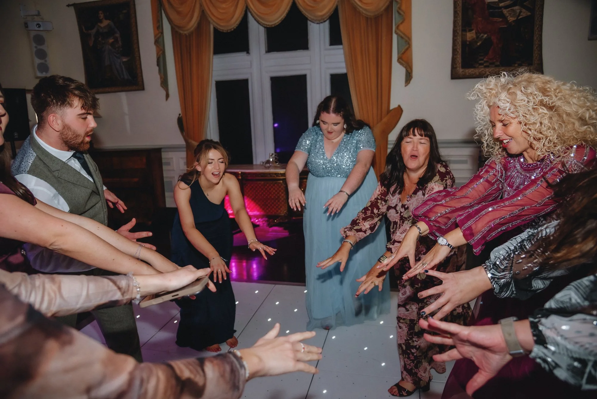 People dancing and having fun at a party in a decorated room with paintings and orange curtains.