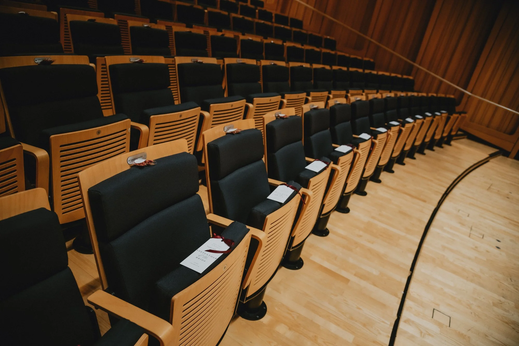 Empty auditorium with wooden seats arranged in rows, some with name tags and ribbons