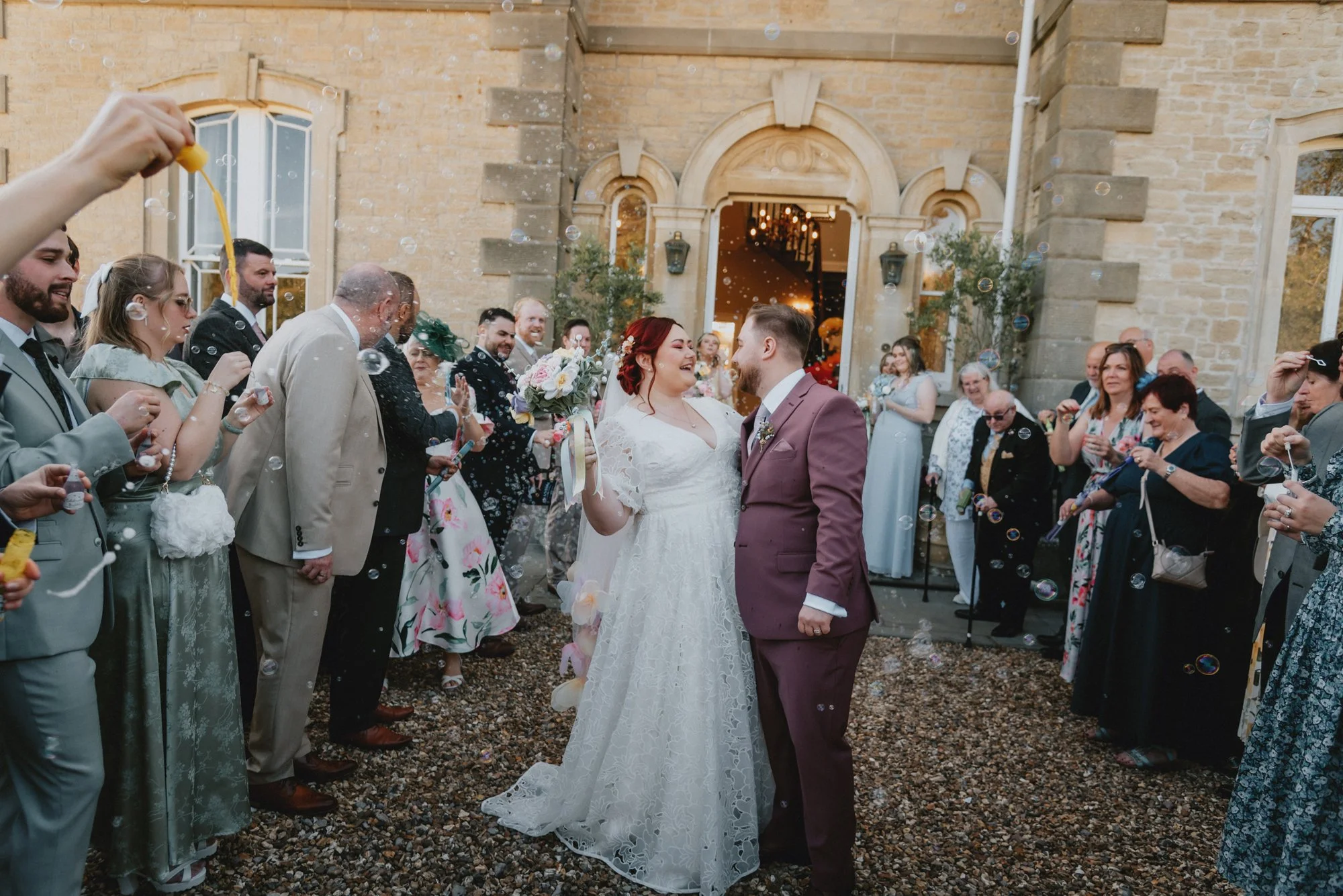 Bride and groom celebrating outside a church, surrounded by friends and family, with bubbles floating in the air.