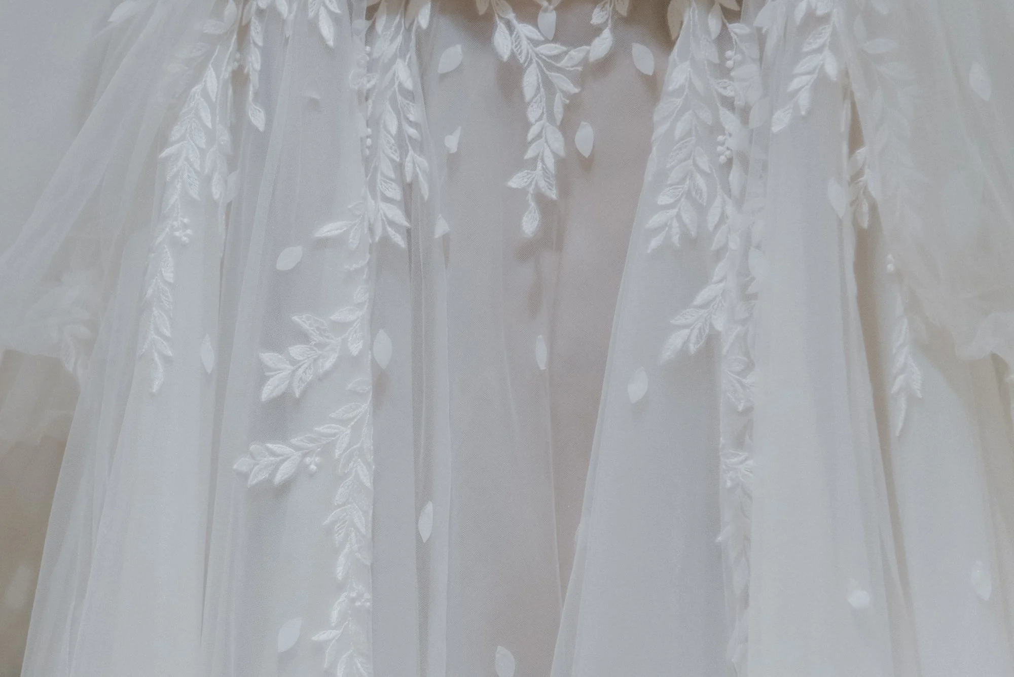 Close-up of a white wedding dress with floral embroidery and sheer fabric.
